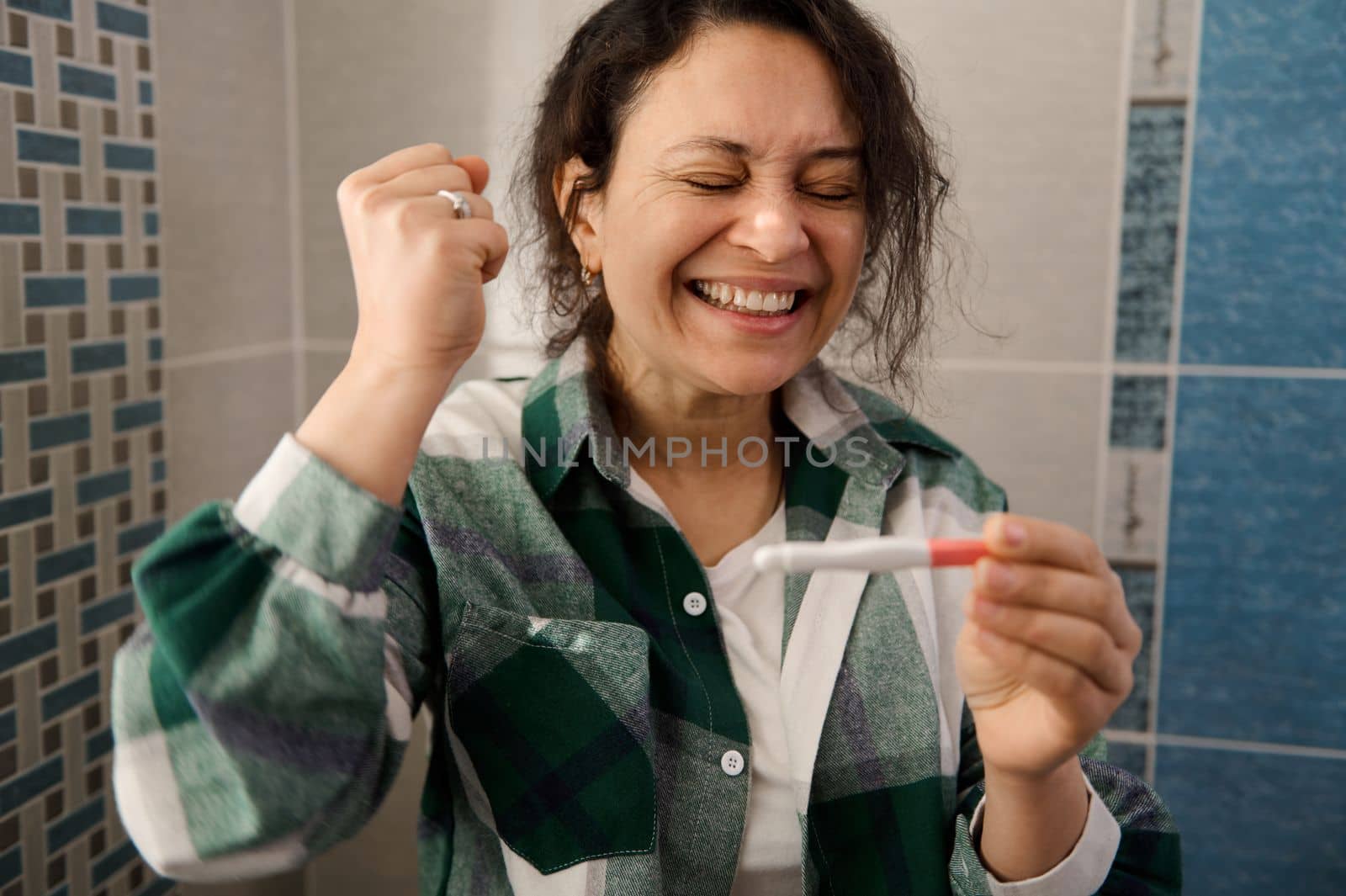 Finally pregnant. Charming multi-ethnic woman rejoicing at positive pregnancy test. by artgf