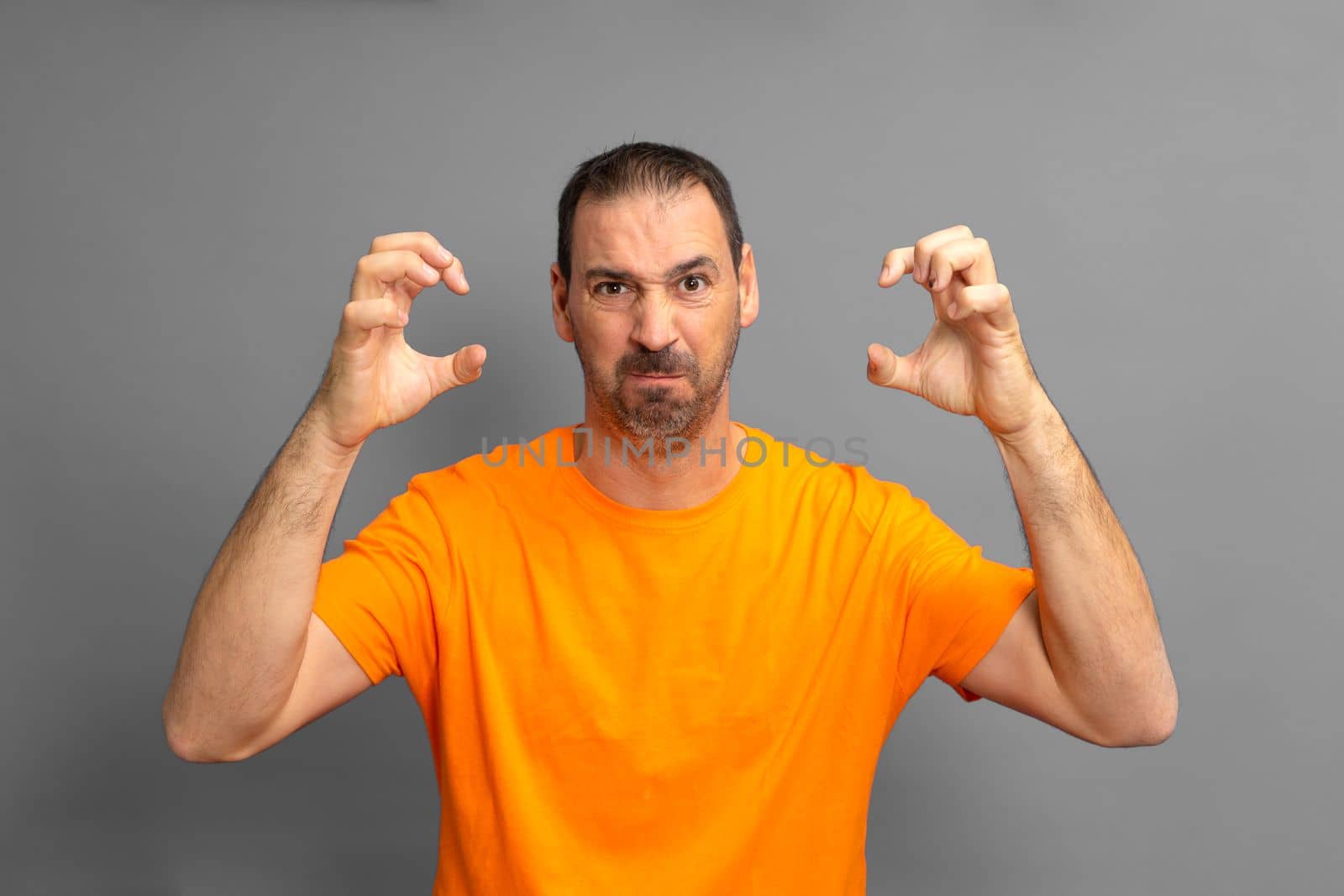 Bearded hispanic man wearing red sweater over isolated gray background doing cat claw gesture because of the extreme anger he has , aggressive expression.