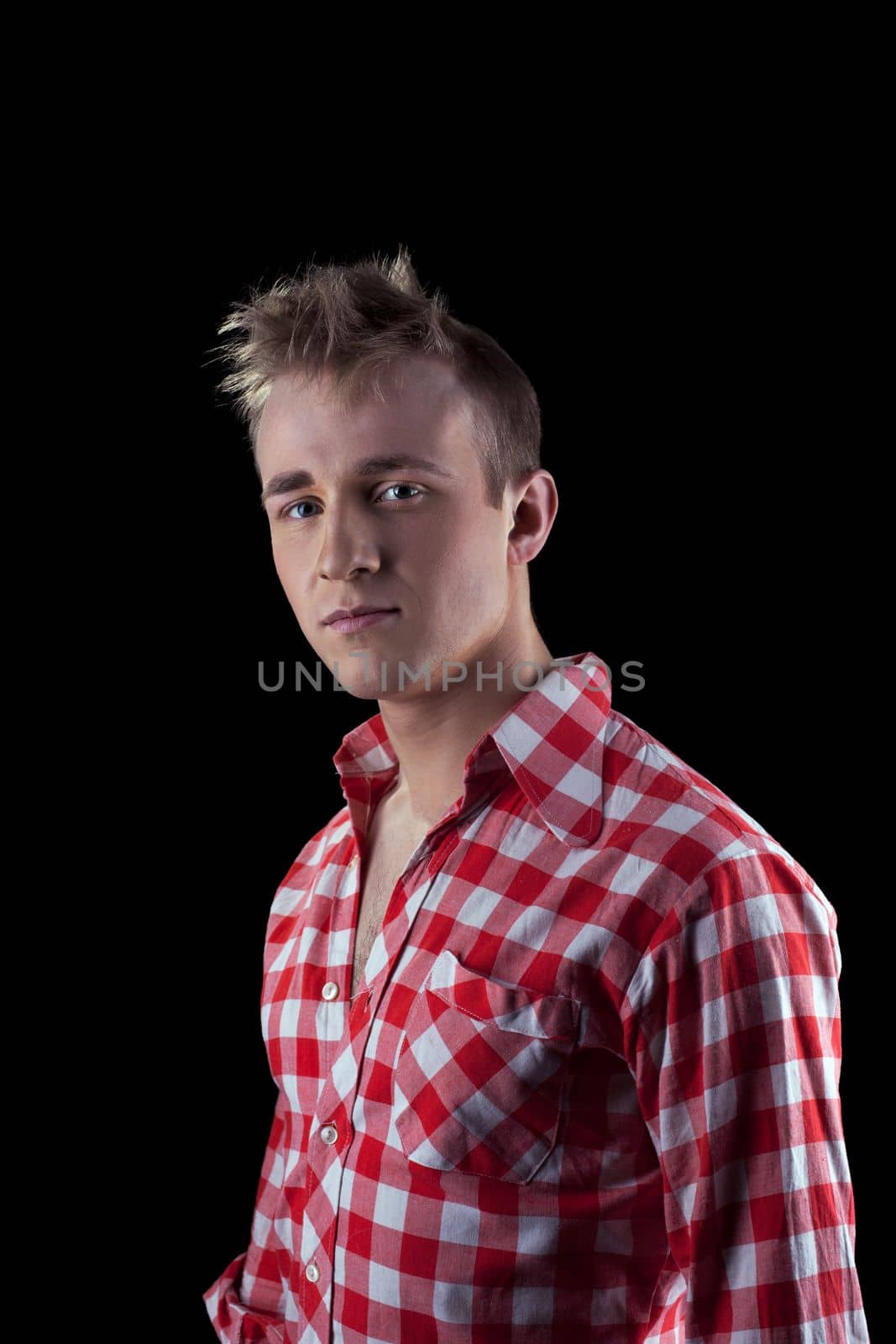 Serious young male in checkered shirt looking at camera while standing against black background