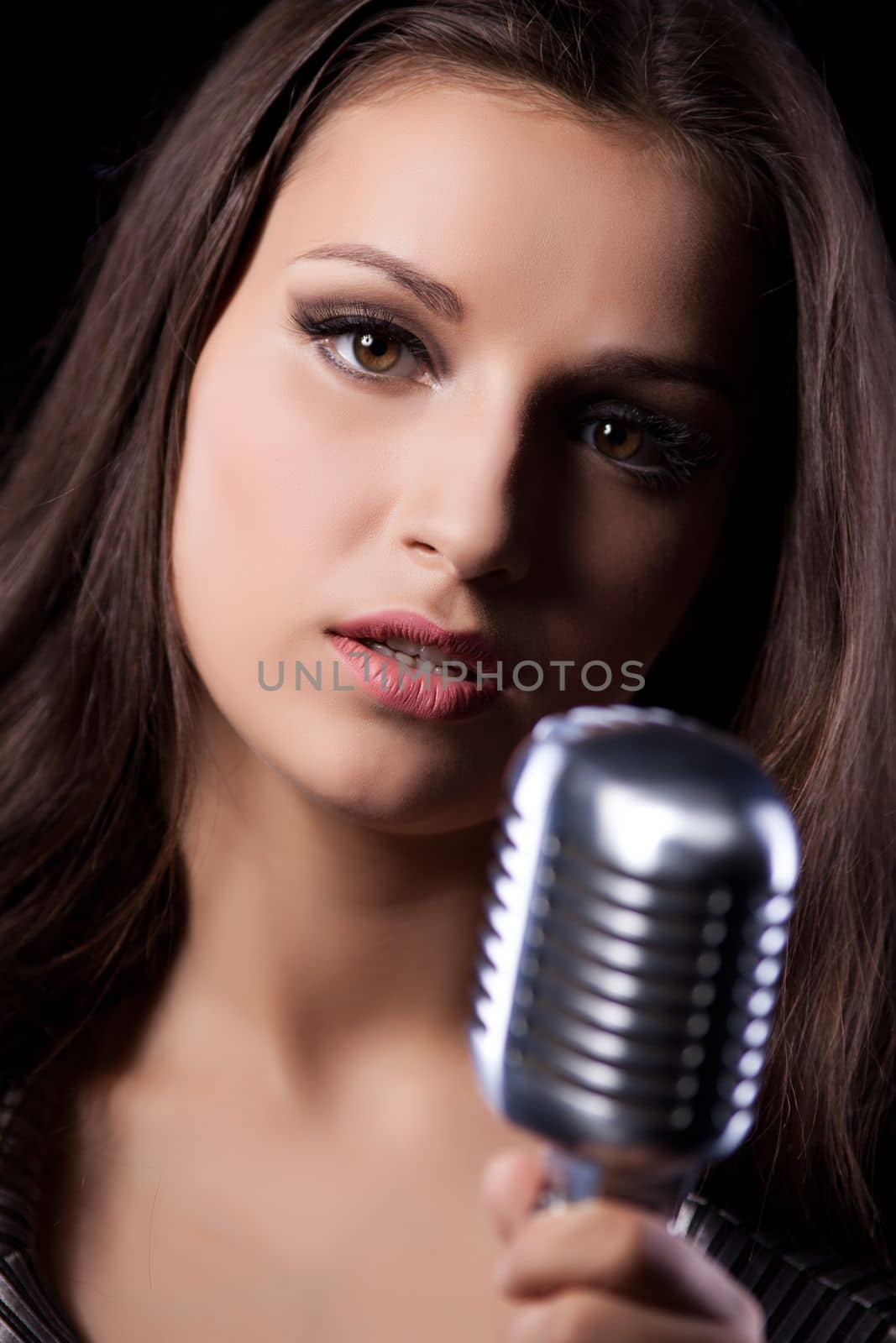 Attractive young female with long hair looking at camera while singing in studio with black background