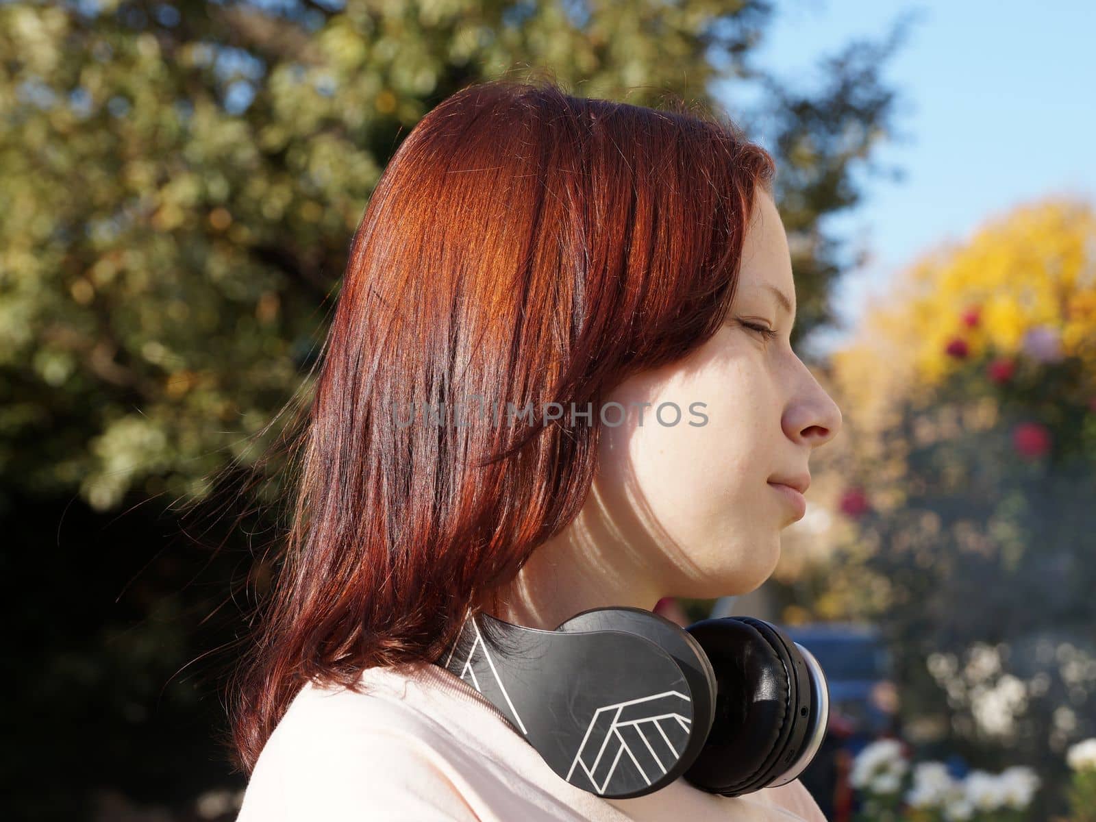 portrait in profile of a red-haired teenage girl with headphones on a background of nature by Annado