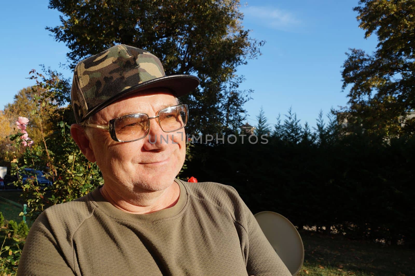 portrait of a smiling man in sunglasses and a baseball cap in the sunlight in the park by Annado