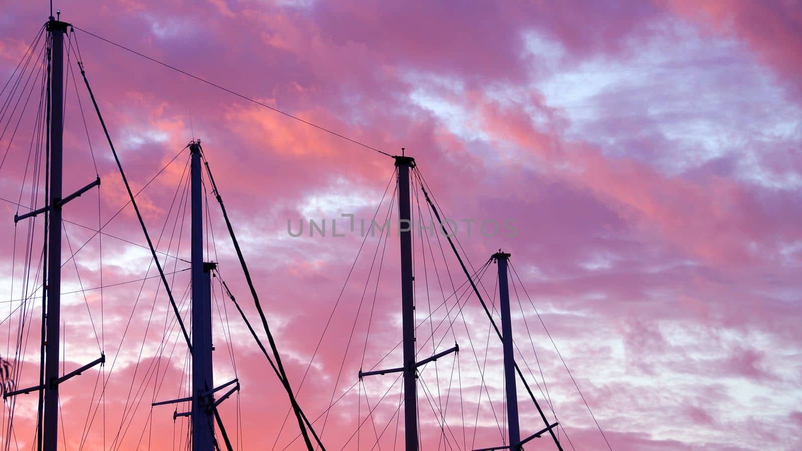 masts of a yacht without sails against the background of a sunset cloudy sky by Annado