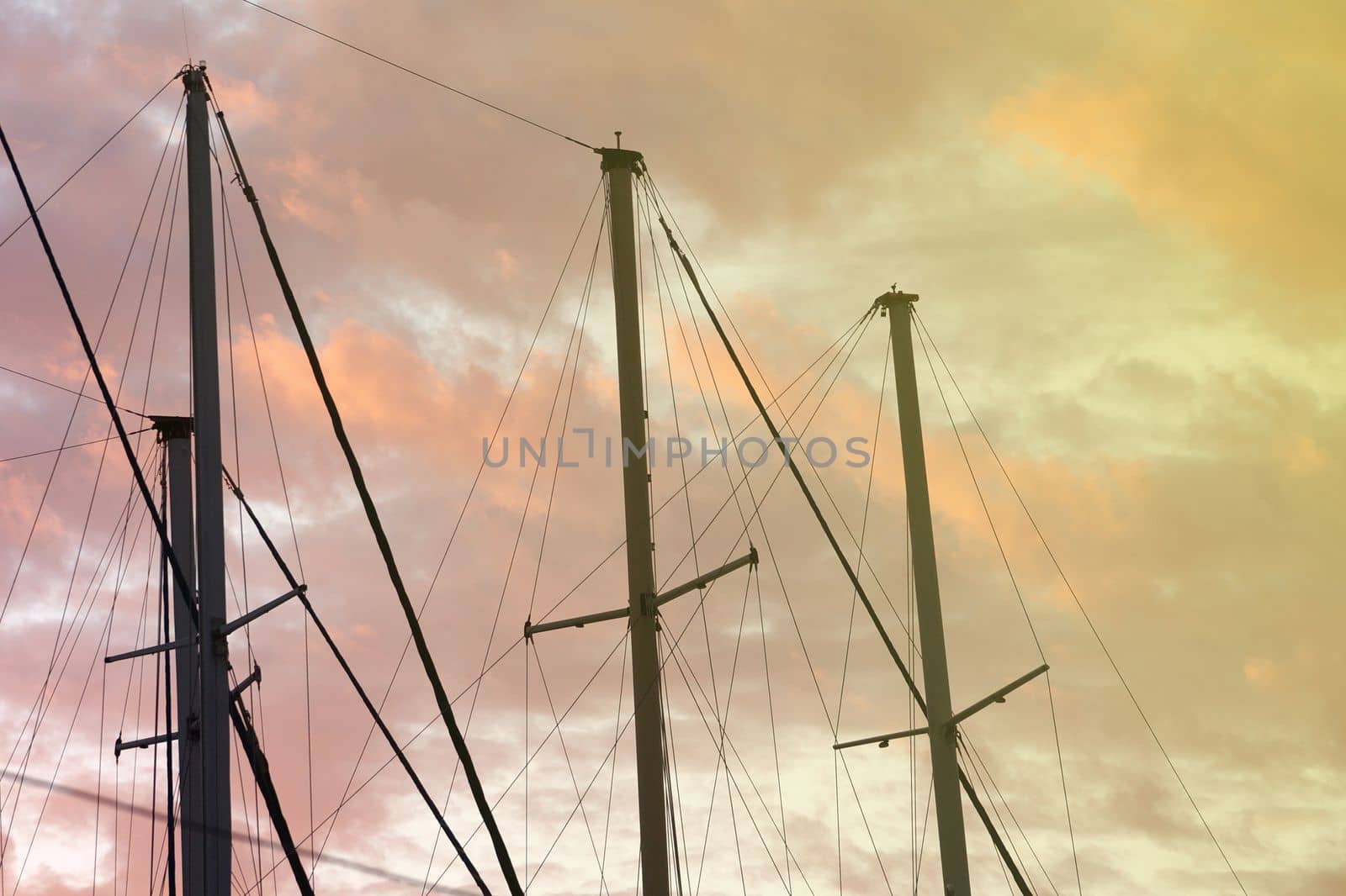 masts of a yacht without sails against the background of a sunset cloudy sky, toned photo