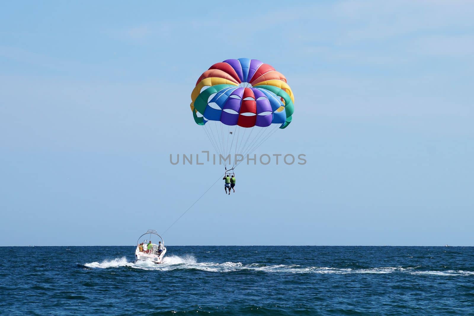 tourists flying on a multicolored parachute tied to a boat by Annado