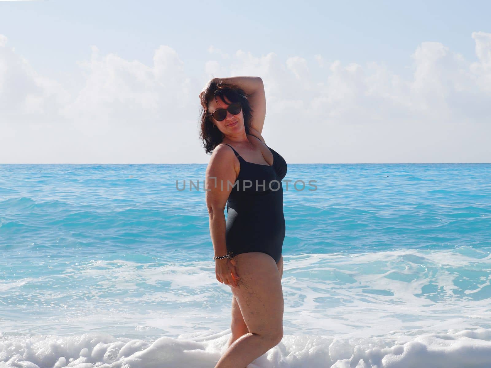 curvy brunette in a black swimsuit in the sea against the background of the sea horizon by Annado