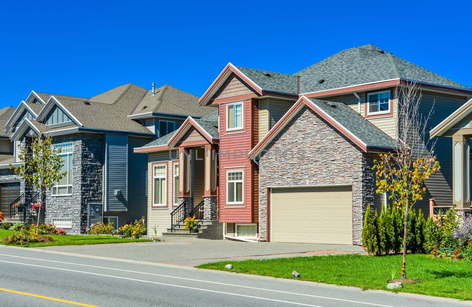 New family house on sunny day with landscaped lawn in front and blue sky background. New house with concrete driveway and asphalt road in front.