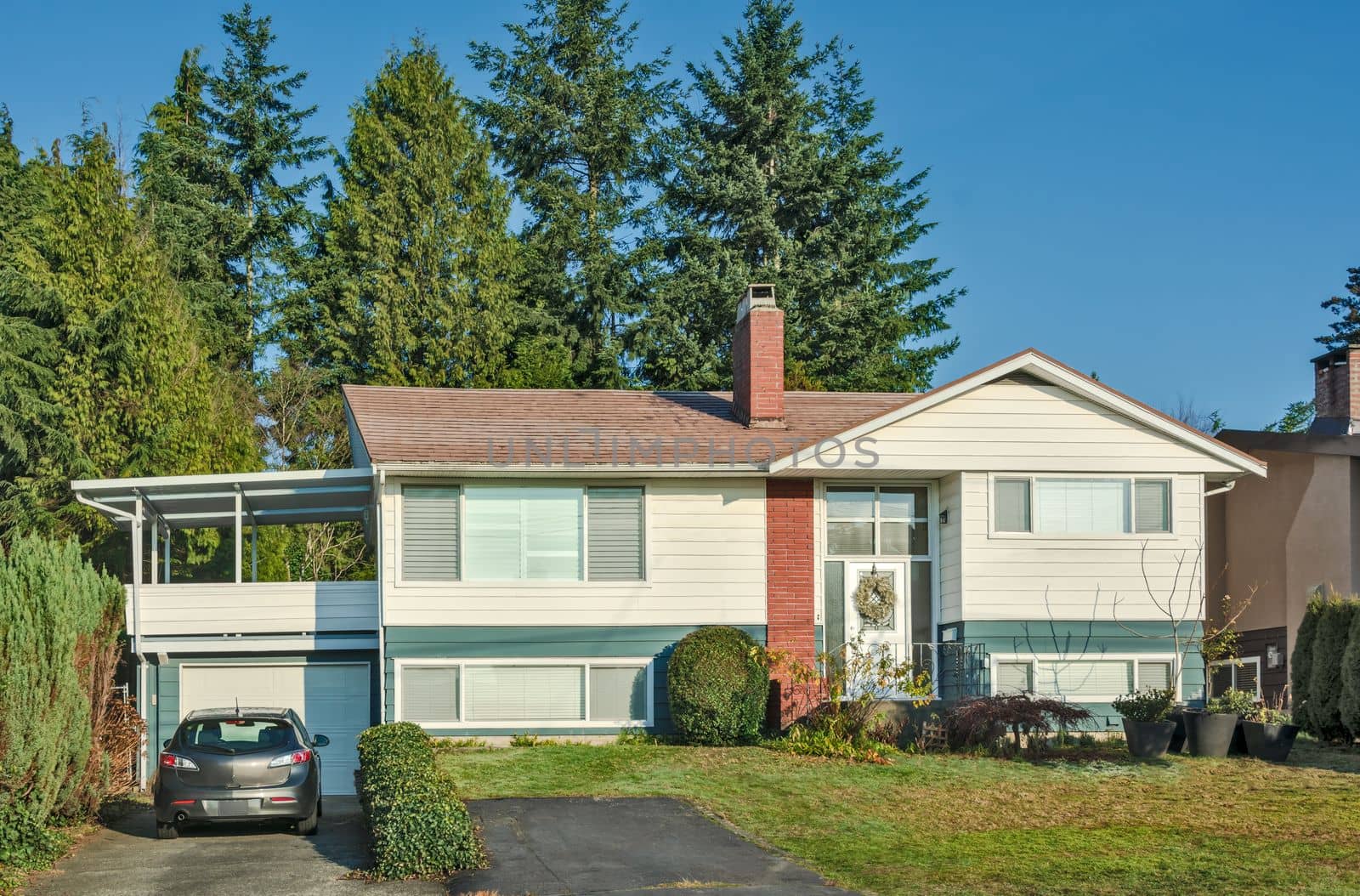 Average residential house in Canada with grey car parked on the driveway. Inexpensive family house on blue sky background