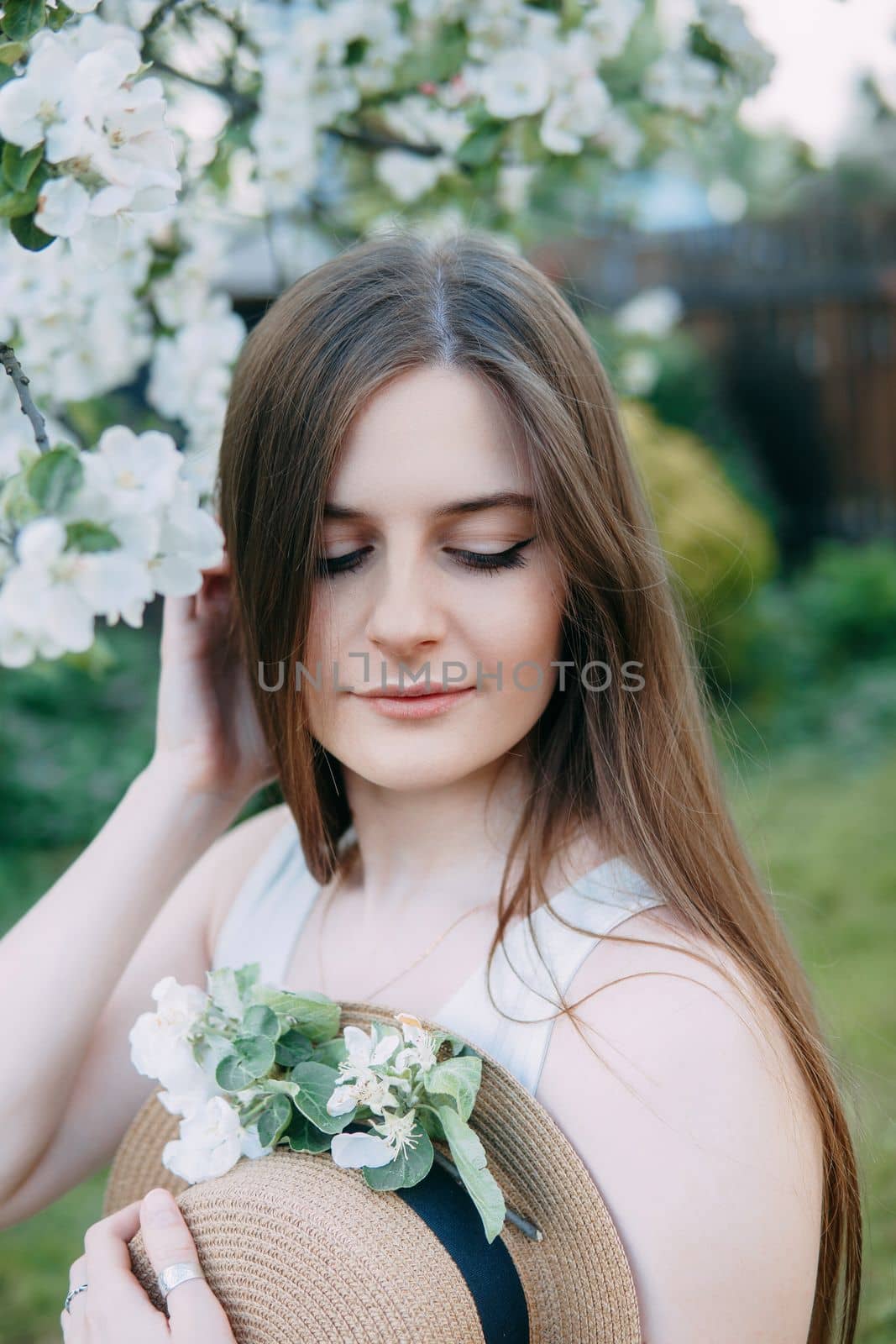 Beautiful young girl in white dress and hat in blooming Apple orchard. Blooming Apple trees with white flowers