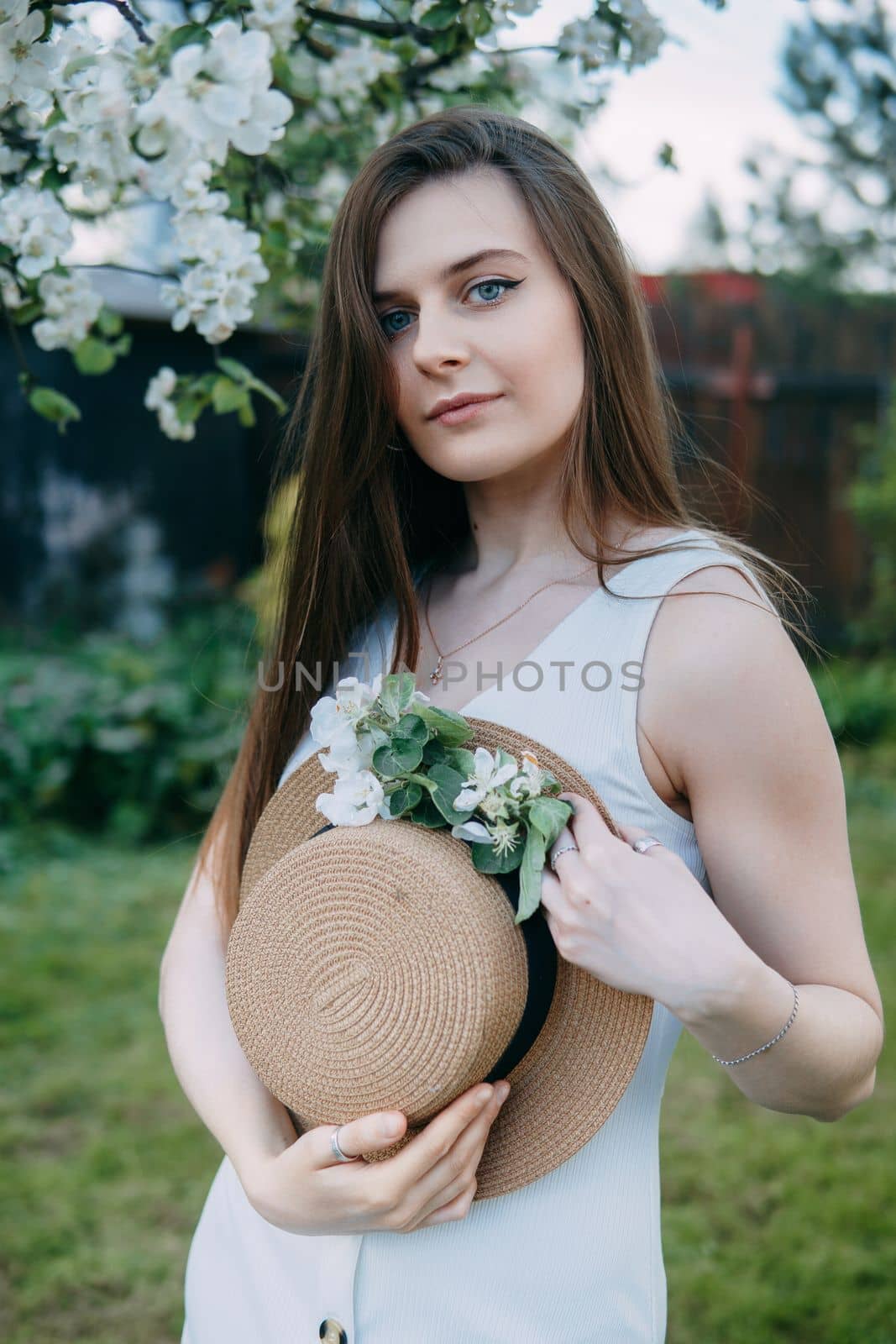 Beautiful young girl in white dress and hat in blooming Apple orchard. Blooming Apple trees with white flowers