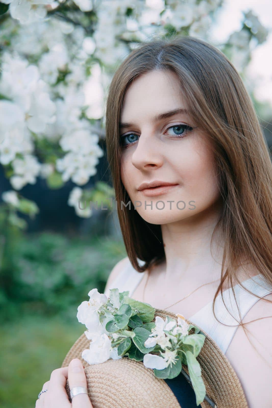 Beautiful young girl in white dress and hat in blooming Apple orchard. Blooming Apple trees with white flowers