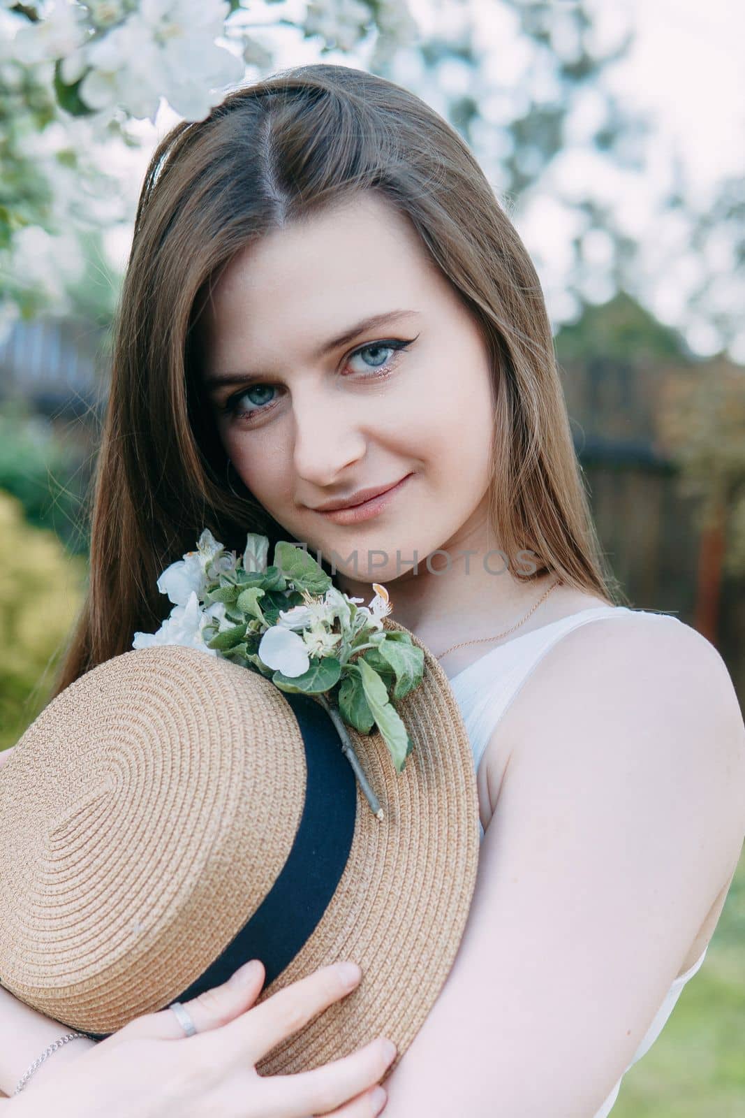 Beautiful young girl in white dress and hat in blooming Apple orchard. Blooming Apple trees with white flowers