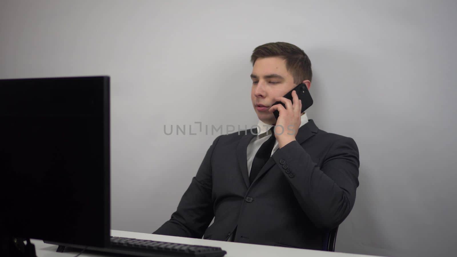 A businessman sits in an office and speaks on the phone. A young IT specialist in a suit is talking on the phone at work. 4k