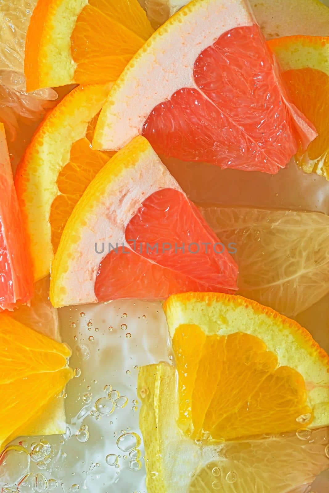 Slices of grapefruit, orange and pomelo in water on white background. Pieces of grapefruit, orange fruit and honey pomelo in liquid with bubbles. Slices of grapefruit, orange fruit and honey pomelo in water. Macro image of fruit in water. Vertical image. Top view, flat design.