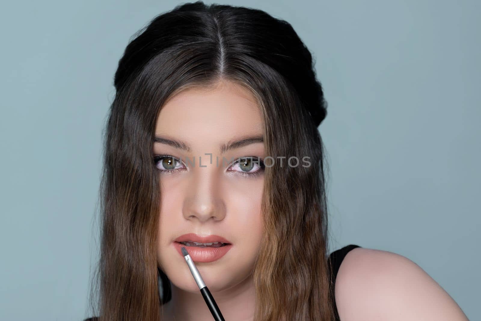 Beautiful young girl with perfect skin and makeup apply pink lipstick on herself. charming young teen using bush painting her lipstick for facial cosmetic concept.