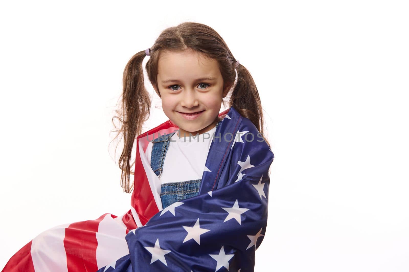Beautiful little citizen of United States of America, a lovely baby girl with two ponytails, wrapping USA flag, isolated over white background. Citizenships. Independence Day. Immigration concept