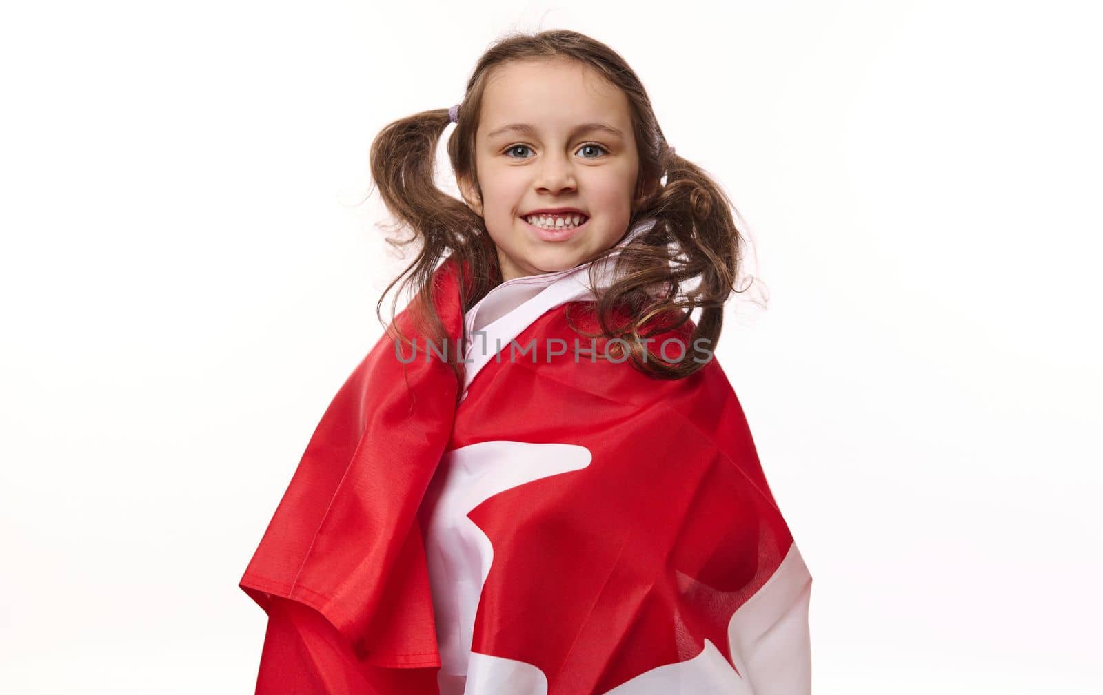 American lovely little child girl, Canadian citizen wrapping flag of Canada, smiling a beautiful toothy smile looking at camera, isolated on white background. Copy ad space. Dominion Day. 1st July