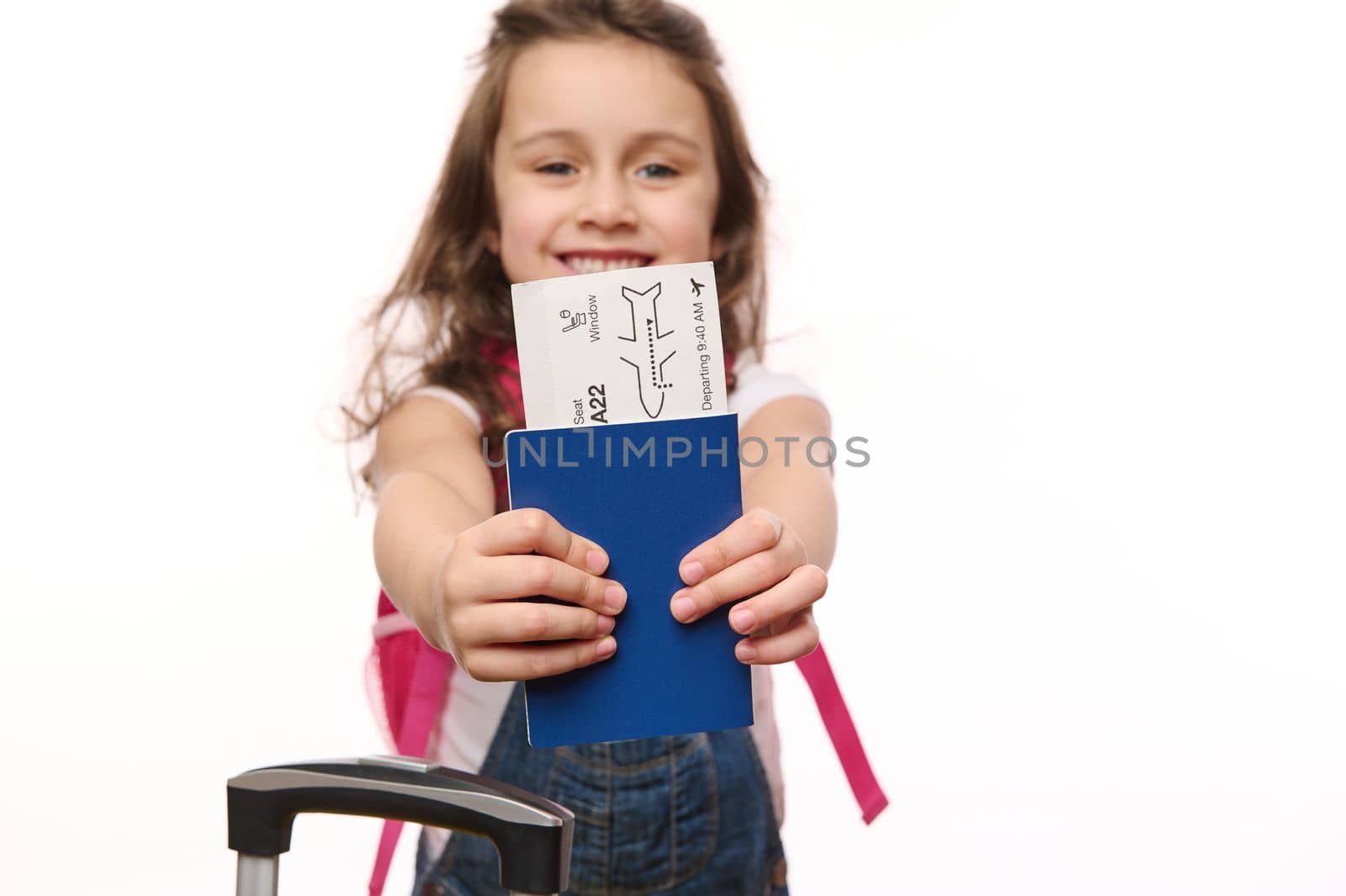Selective focus on boarding pass or flight ticket in the hands of blurred cutely smiling baby girl, isolated over white background with free space for advertising text. Travel by air. Journey. Tourism
