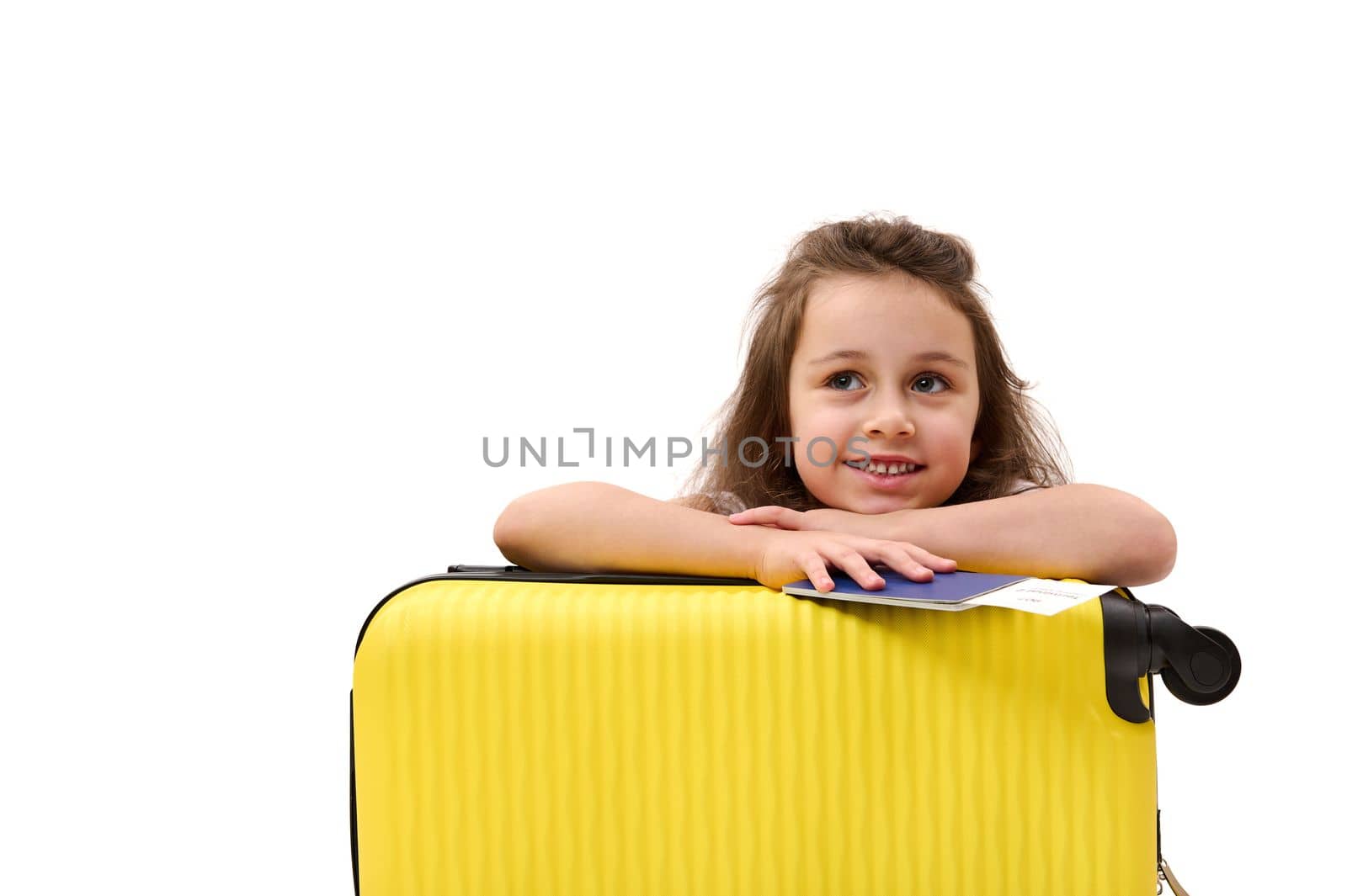 Adorable little passenger girl, with boarding pass and suitcase, traveling abroad for the weekend, smiling toothy smile, dreamily looking away at advertising space. Tourism Tourney Air travel concept