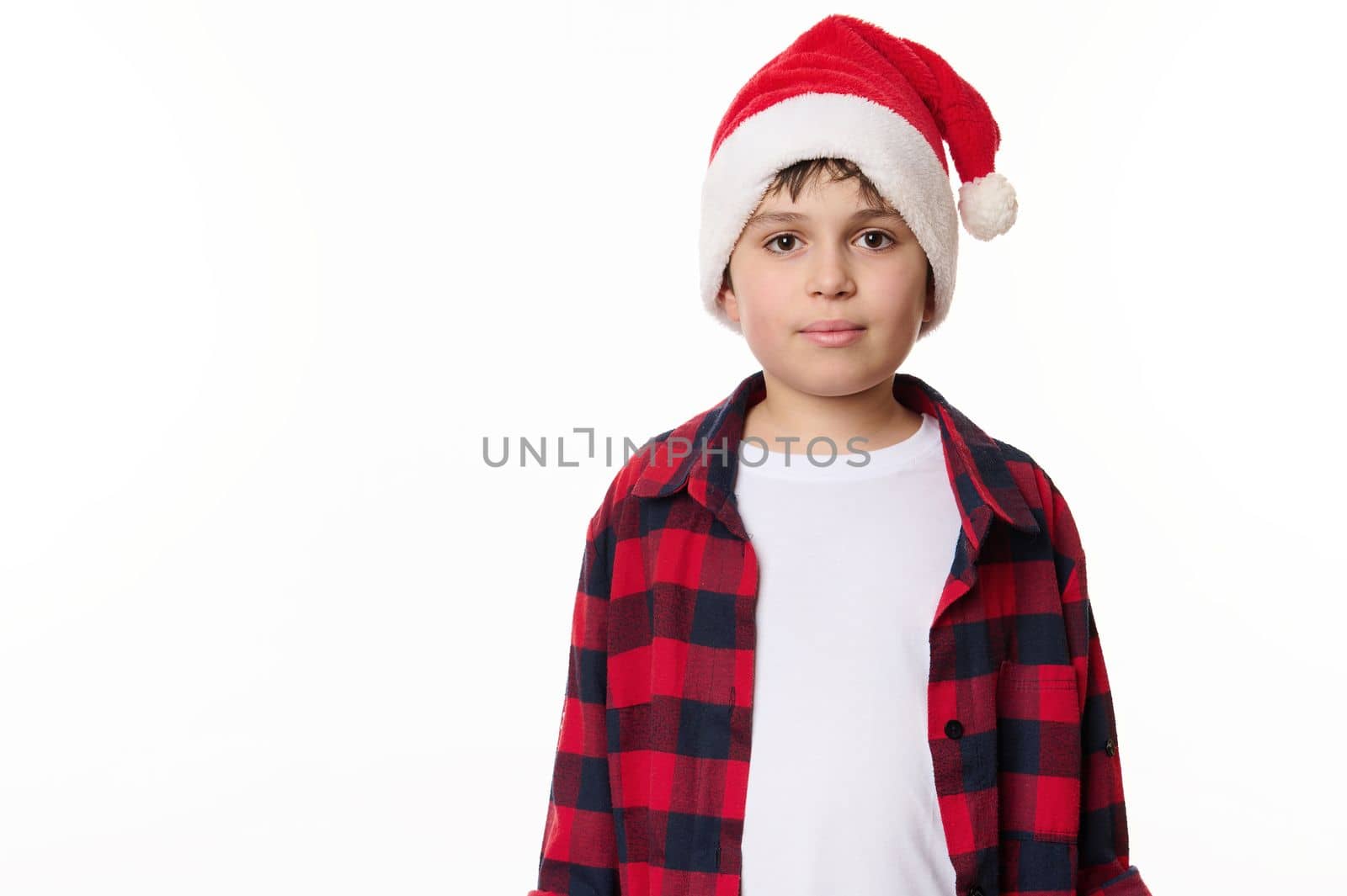 Half-length portrait of handsome Caucasian teenage boy in Santa hat, looking confidently at camera, isolated on white background. Copy space for advertising text. Merry Christmas and Happy New Year