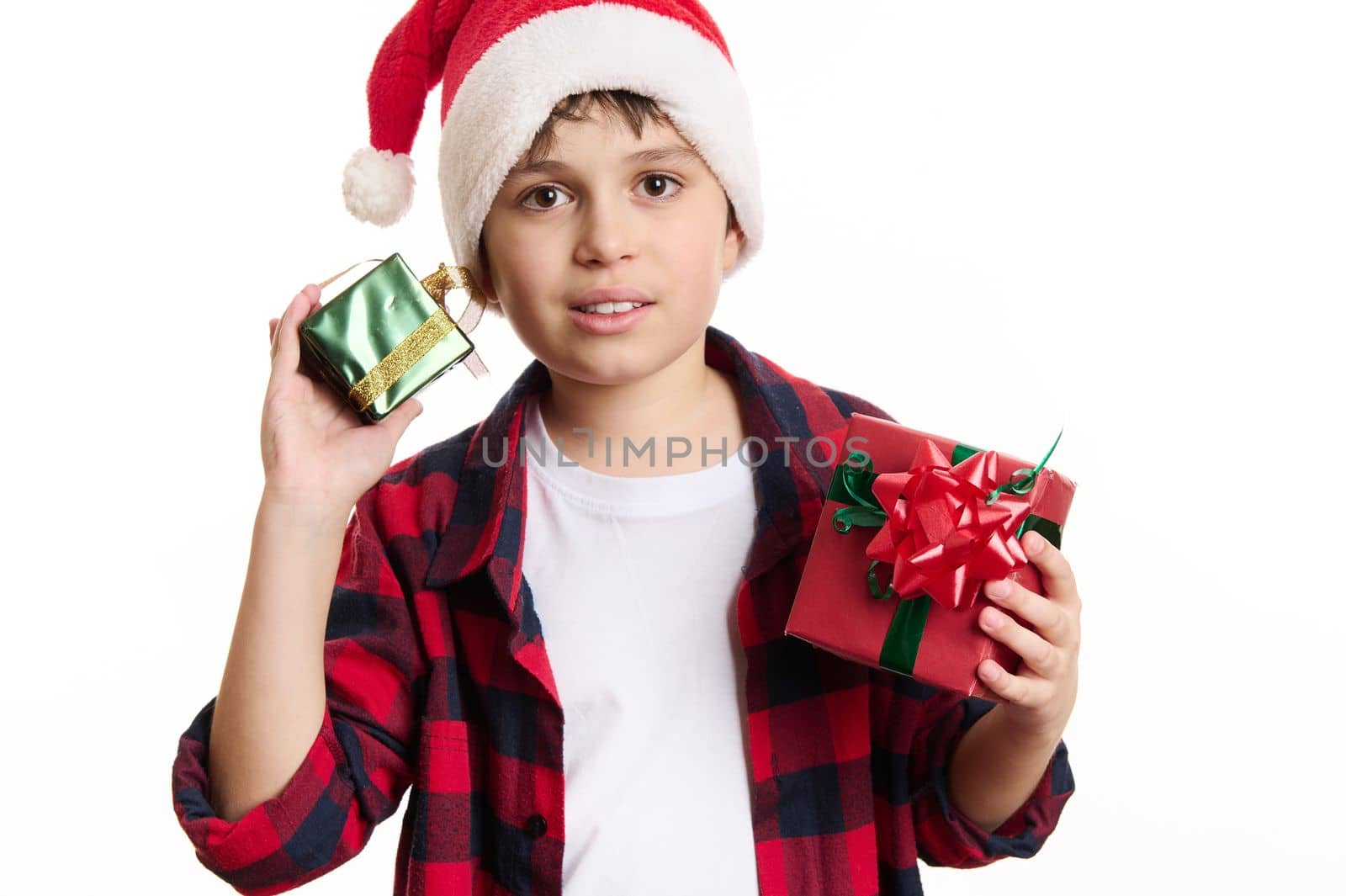 Half-length portrait: handsome Caucasian teenage boy in Santa hat, holding Christmas gifts, looking confidently at camera, isolated on white background. Copy space for advertising text. Happy New Year