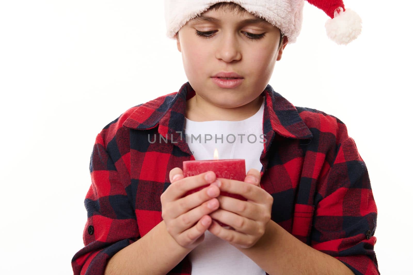 Close-up portrait of a handsome preteen Caucasian boy with a lit candle, isolated on white background. Adorable child making wish. Merry Christmas, Happy New Year and winter holidays. Copy ad space