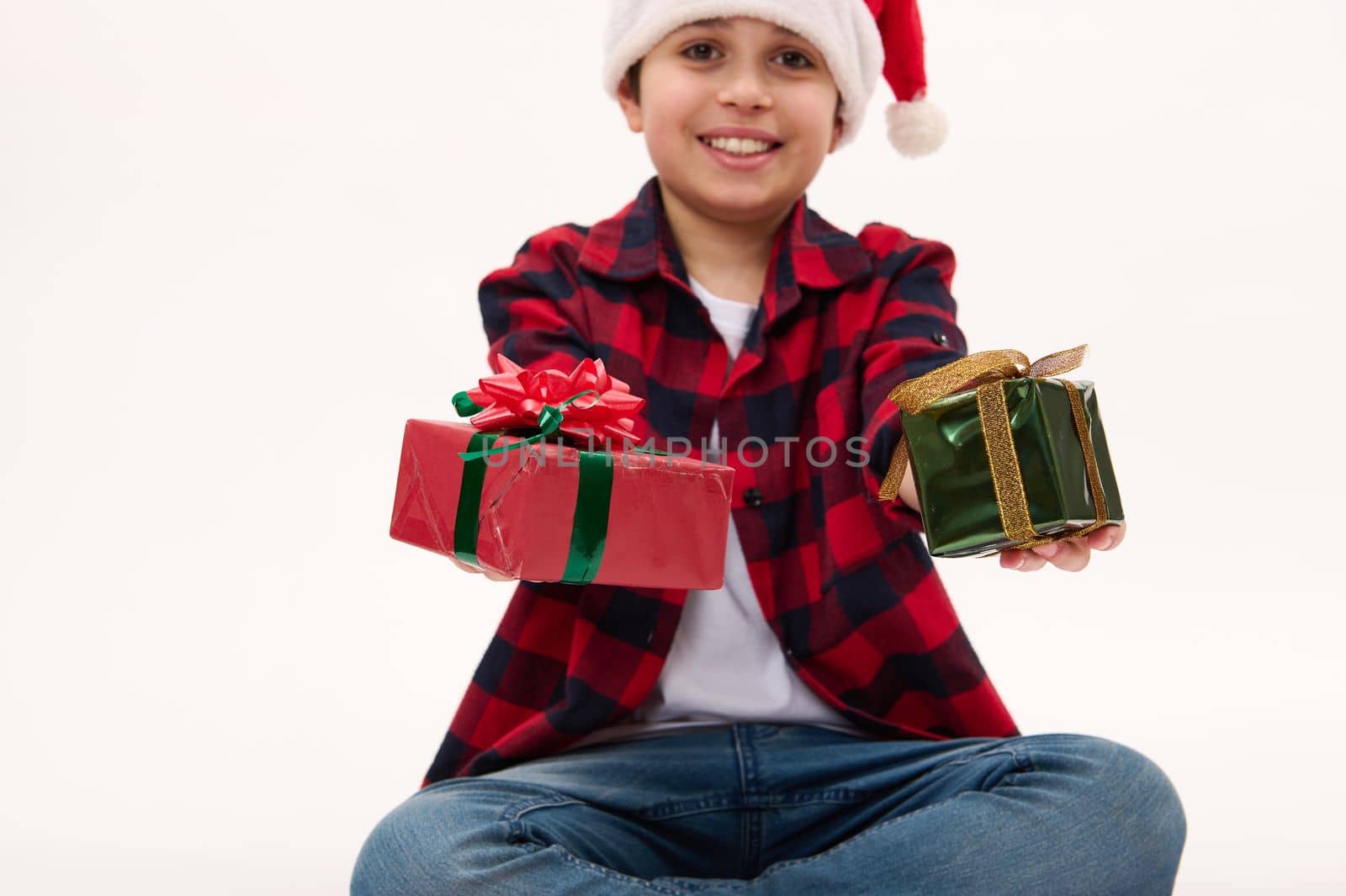 Selective focus on beautiful happy presents for Christmas or New Year, in the hands of a blurred charming preteen boy wearing Santa, isolated over white background with copy ad space. Boxing Day