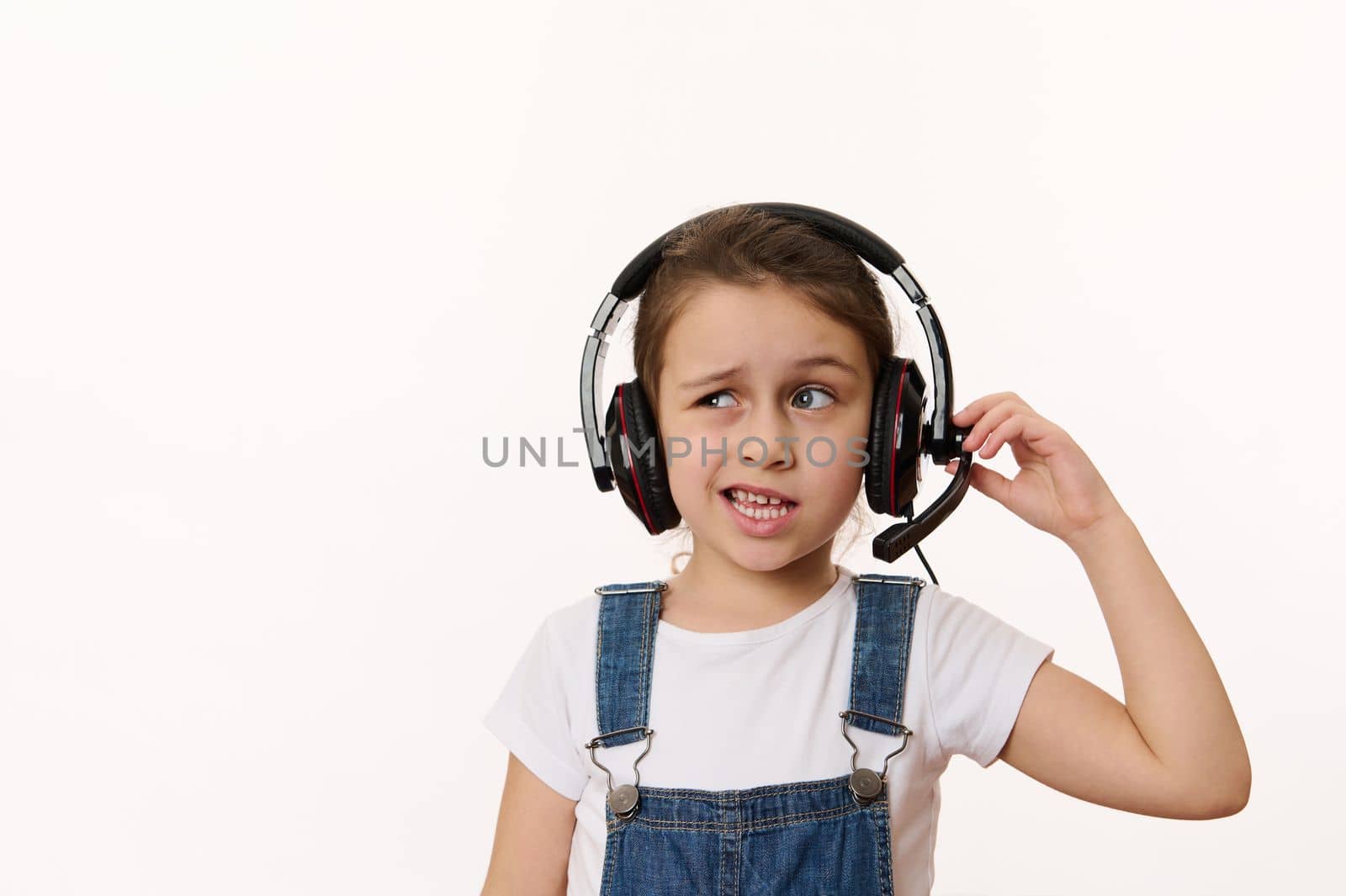Adorable little child, smart school girl wearing headphones has a video conference during an online lesson, isolated over white background. Copy advertising space. Back to school. Internet learning