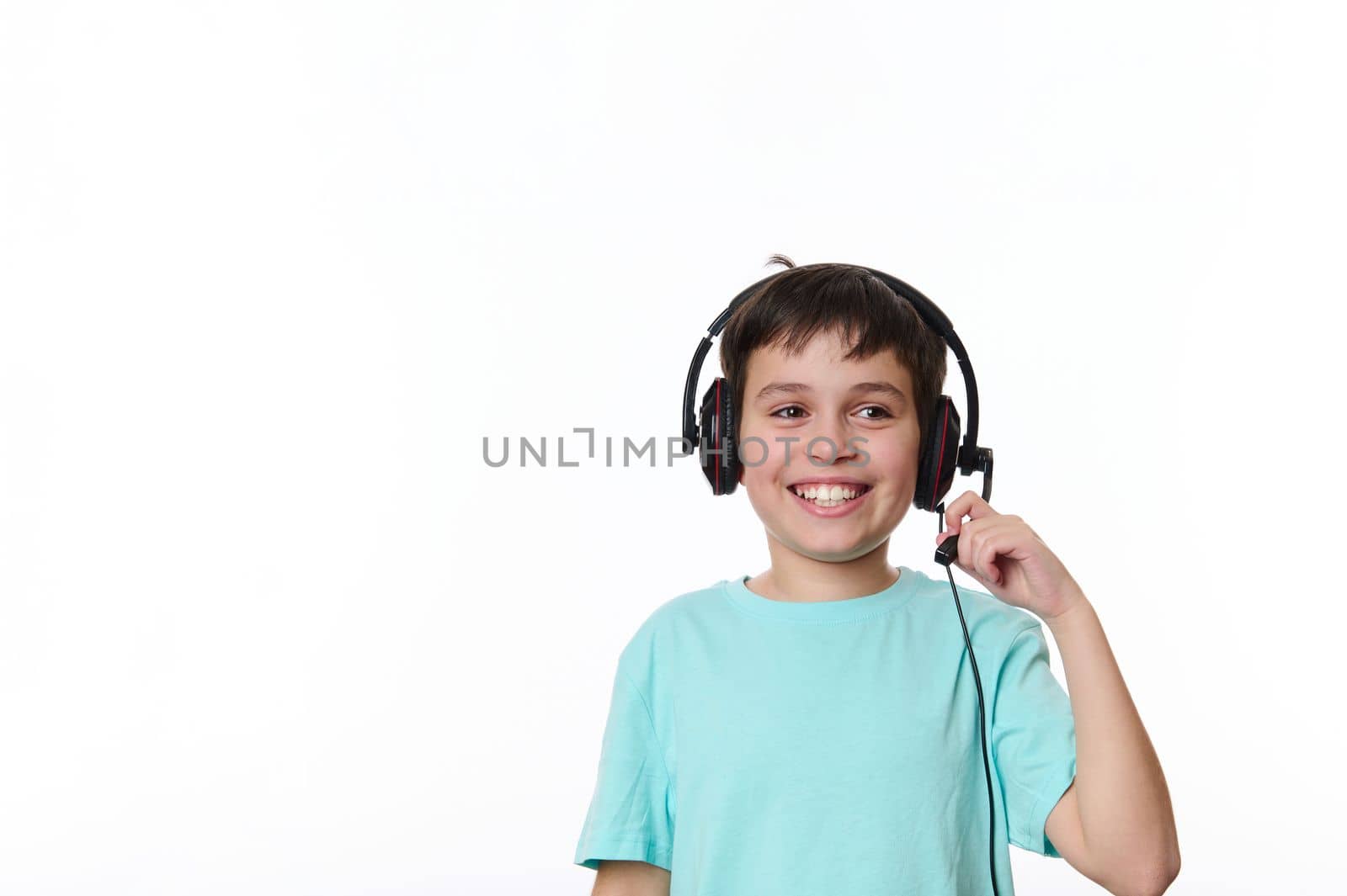 Smart Hispanic teenage child, a school boy wearing audio headset, cutely smiles cheerful toothy smile, isolated on white background. Online meeting, distance learning, internet education. Video call.