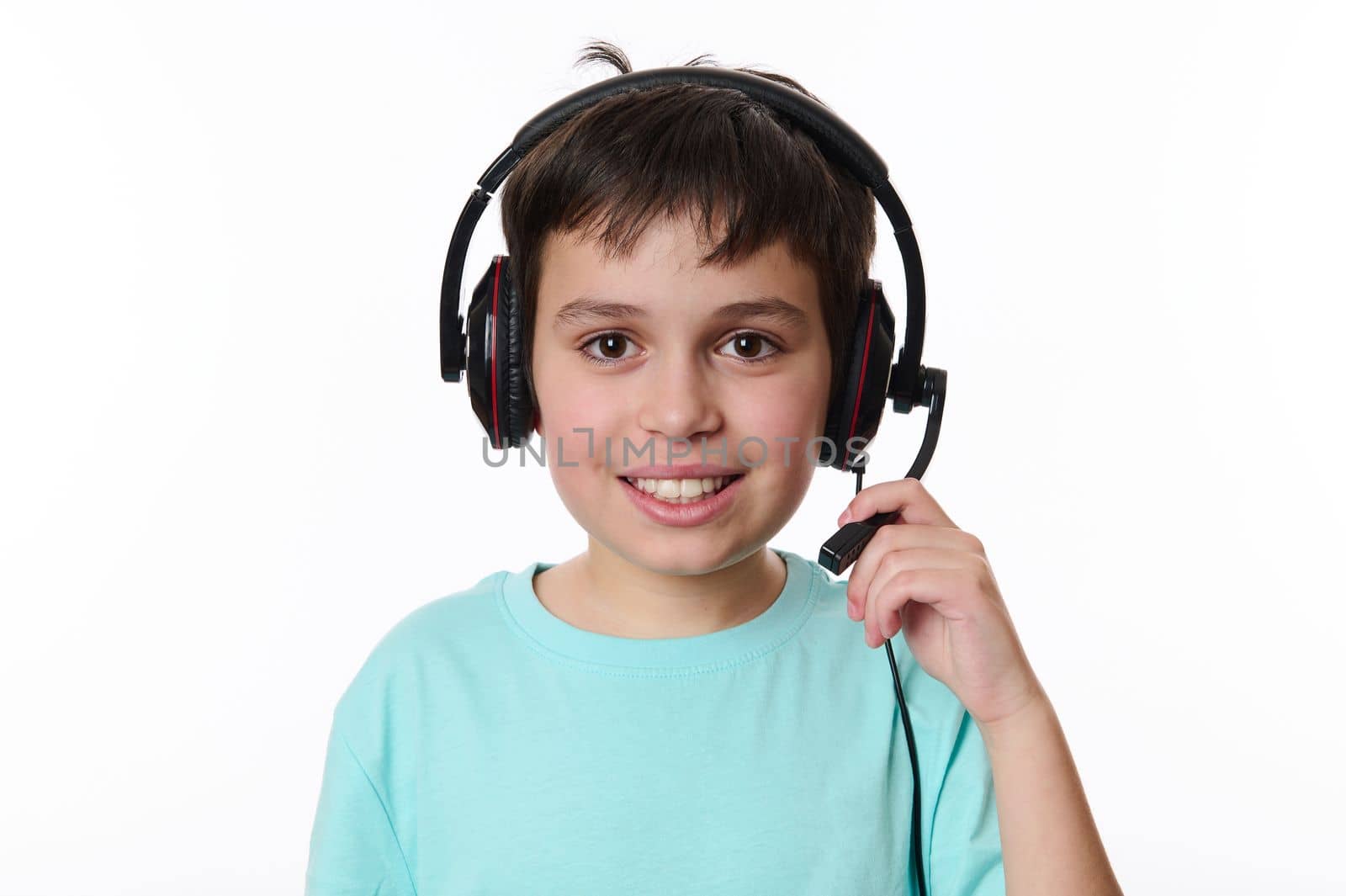 Close-up portrait of a handsome Caucasian smart teenage school boy, wearing audio headset, ready for online lesson, smiling cutely looking at camera, isolated over white background. Copy ad space