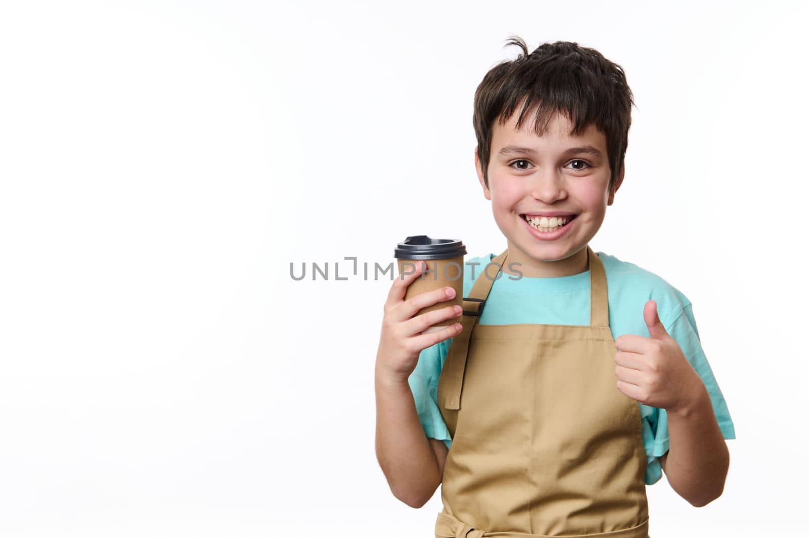 Happy Caucasian teenage boy, bartender barista holding, selling a takeaway hot coffee drink in a paper cup, showing thumb up, isolated over white background with copy space for your promotional text