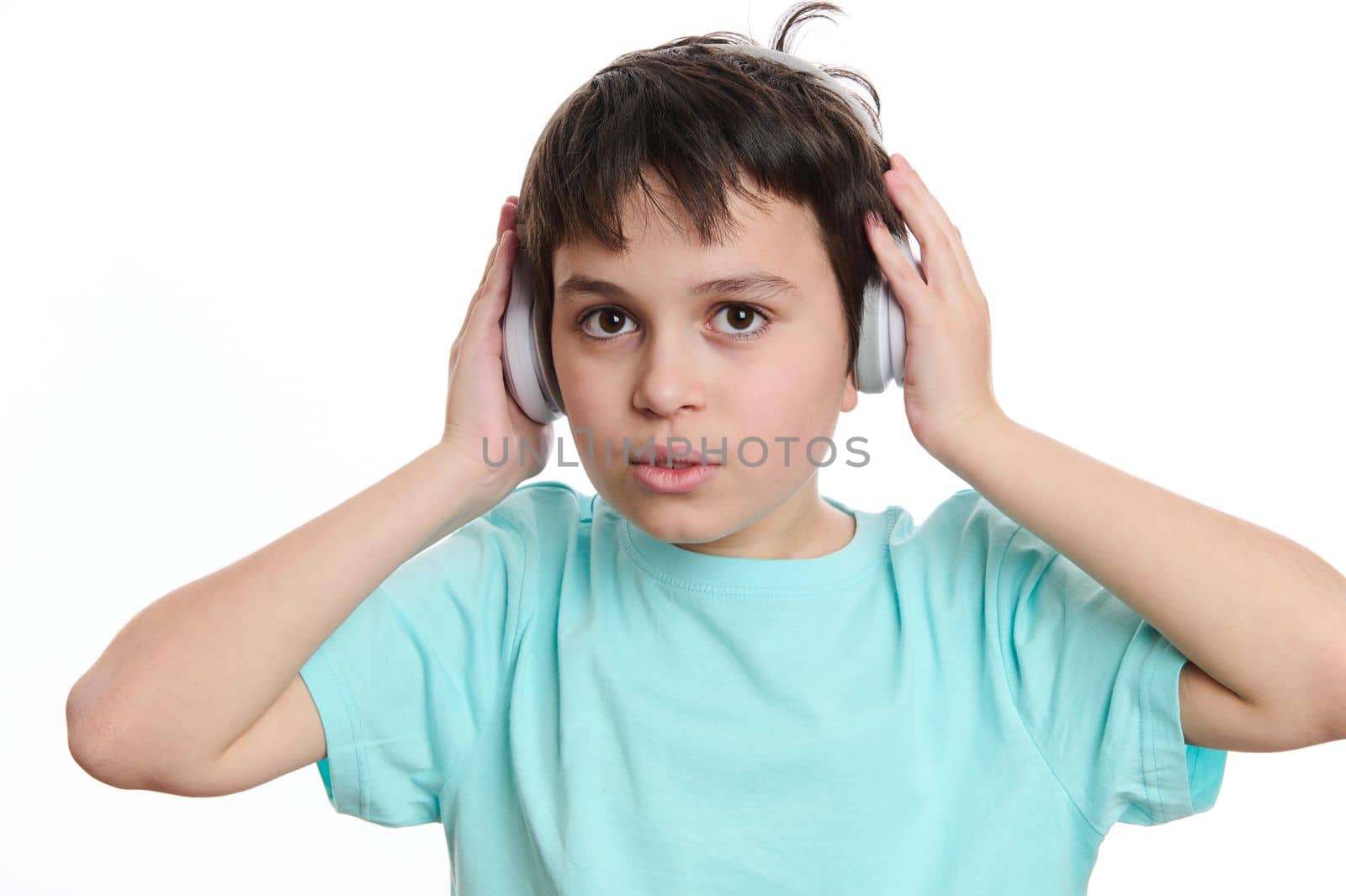 Close-up portrait handsome multi-ethnic teenage boy in turquoise t-shirt, puts on wireless headphones, looking at camera, isolated on white background with copy advertising space for promotional text