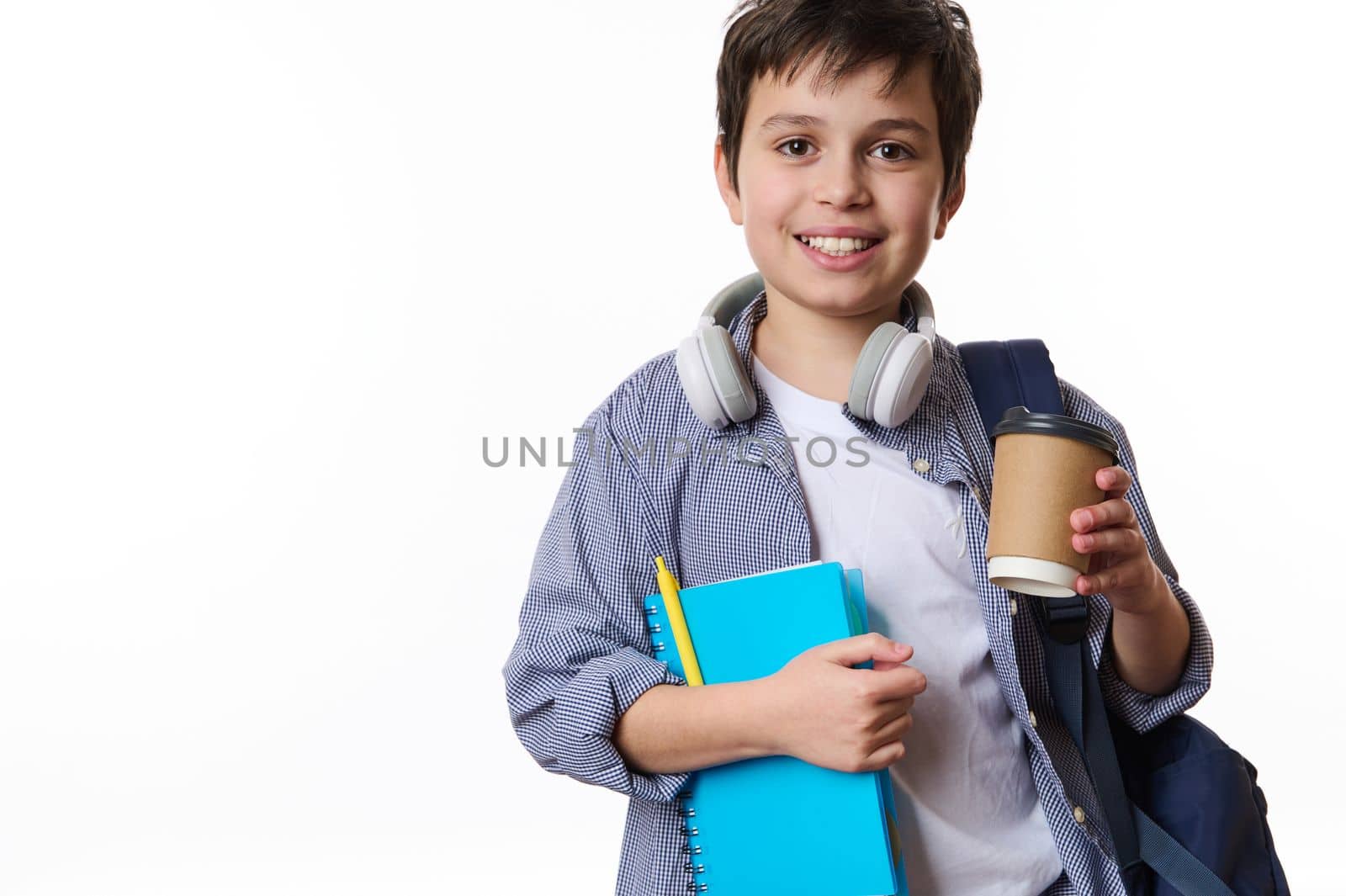 Caucasian smiling teenage schoolboy with school supplies and backpack, holding out a takeaway drink in disposable paper cup, looking at camera, isolated on white background. Copy advertising space
