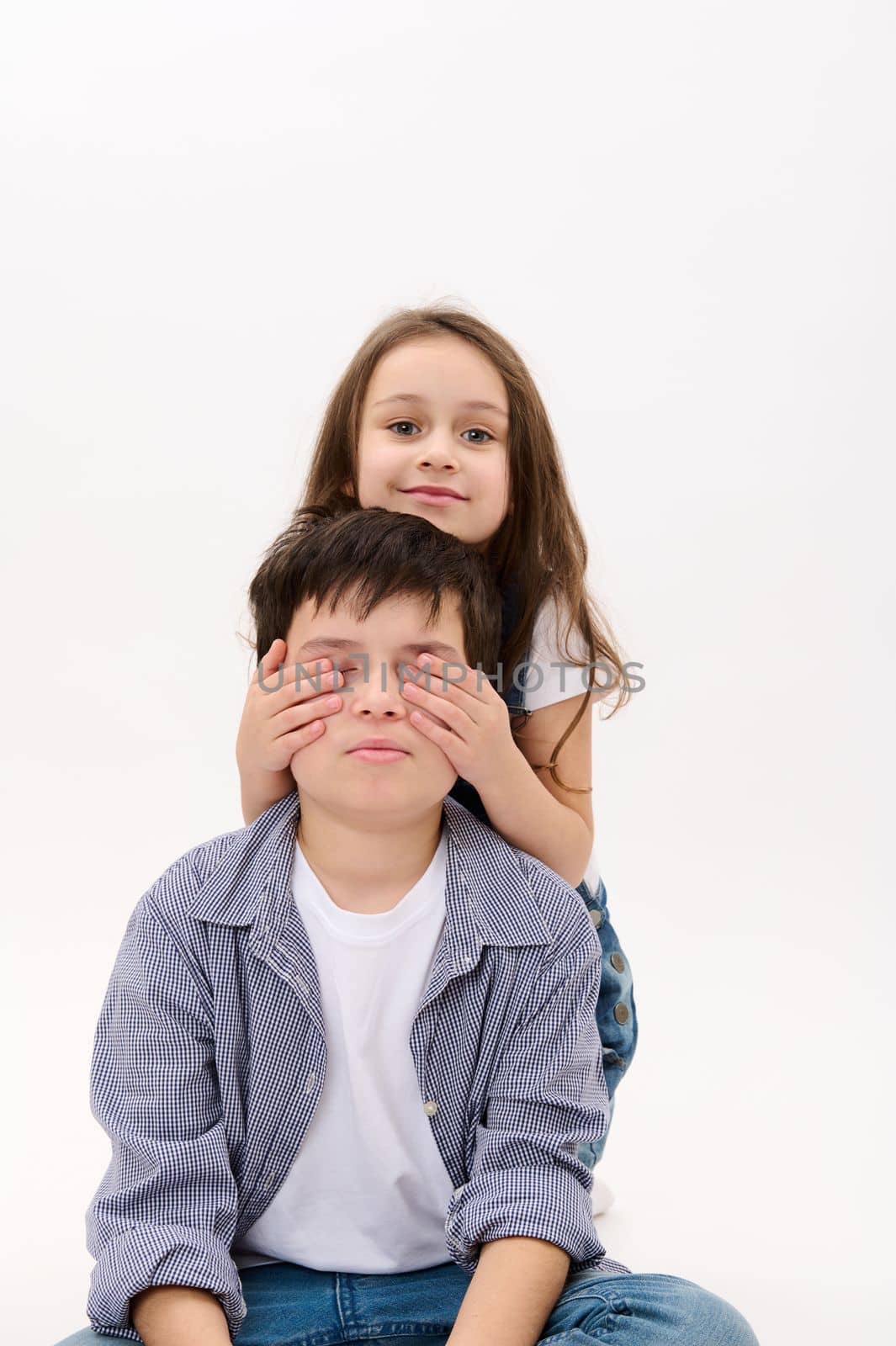 Lovely baby girl - little sister hugging her brother - a teenage boy - from the back, isolated over white background. International Children's Day celebration. Kids rights. Happy family relationships