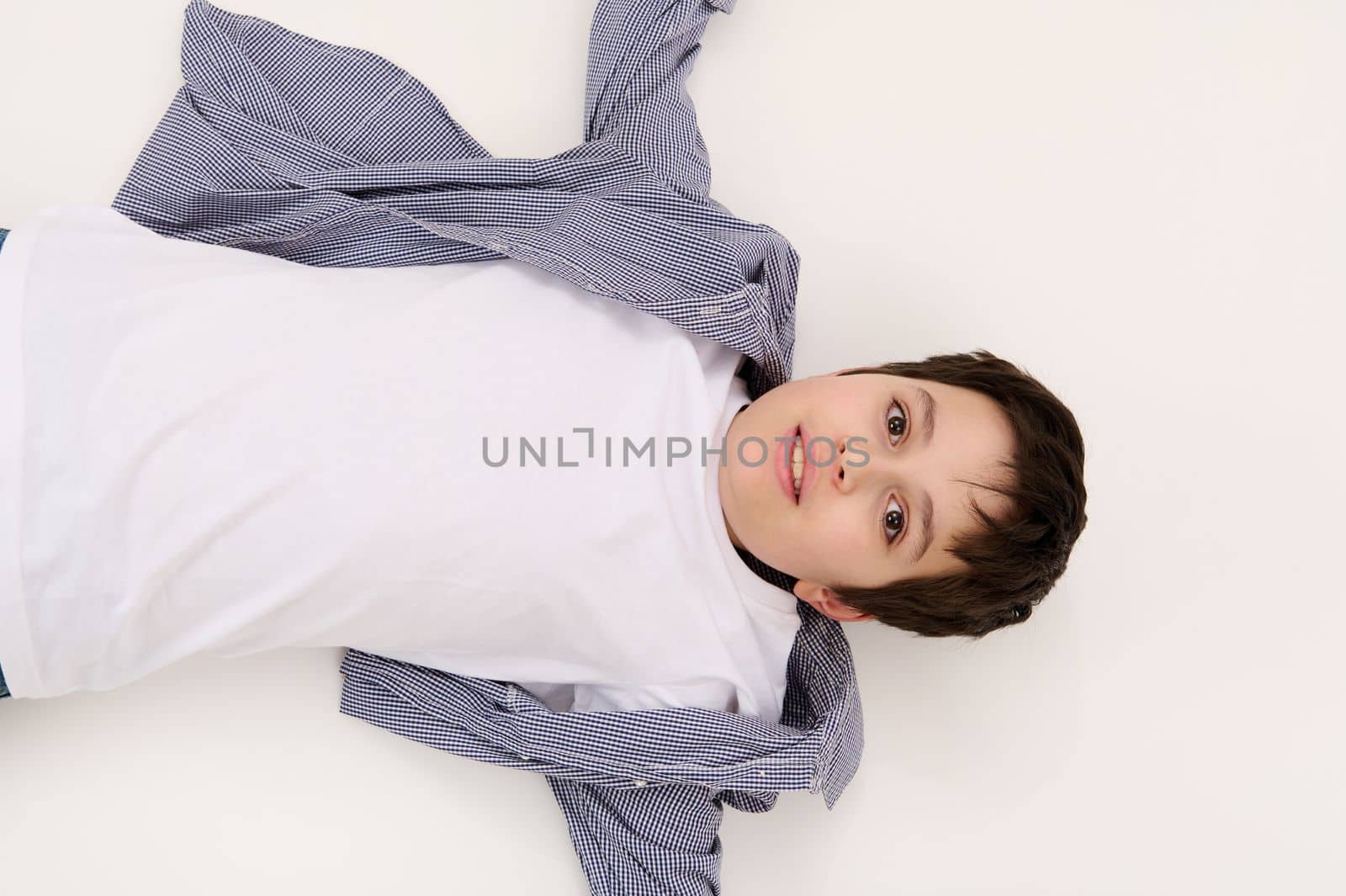 Top view multi-ethnic dark-haired brown-eyed adorable teen boy in white t-shirt and blue shirt, looking at camera, isolated on white background with free advertising space for promotional text