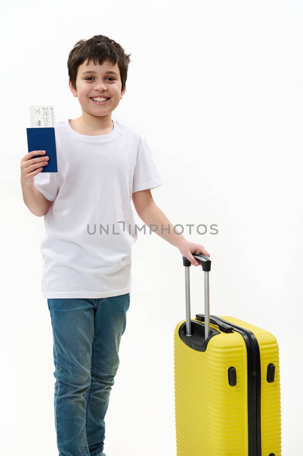 Travel concept. Happy multi-ethnic child boy, teenage traveler going on summer vacations, walking with suitcase, air ticket and passport, isolated on white background, free space for your advertising
