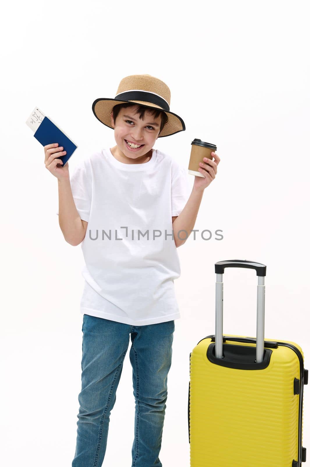 Teenage boy excited about summer vacation trip. Joyful teenager with travel bag, disposable paper cup of hot drink and boarding pass waiting for flight, isolated on white background. Vacation concept