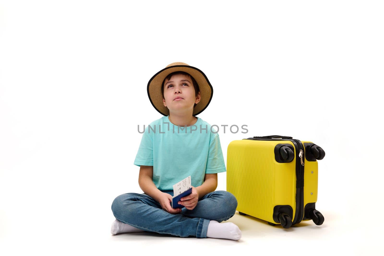 Isolated portrait on white background of multi-ethnic pre-adolescent passenger, teenage traveler boy with yellow suitcase, dreamily looking up at ad space. Air travel. Tourism. Journey. Travel concept