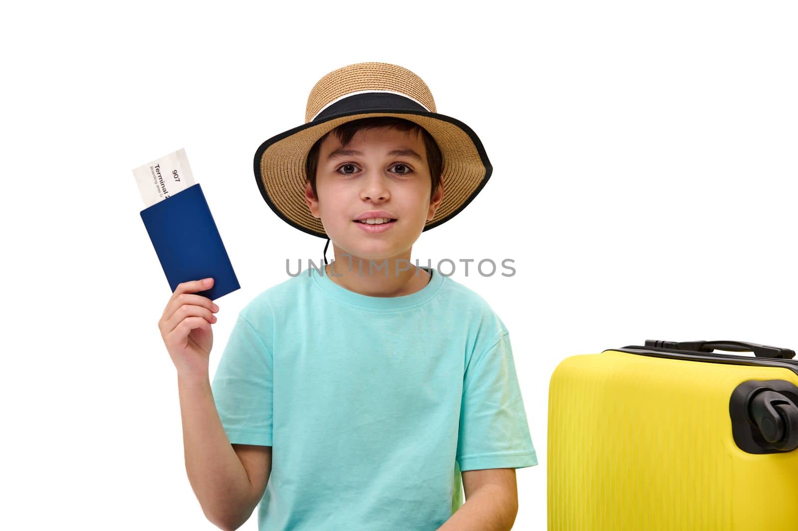 Adorable preteen traveler boy in blue t-shirt and straw hat, going for summer vacations, showing boarding pass to camera by artgf