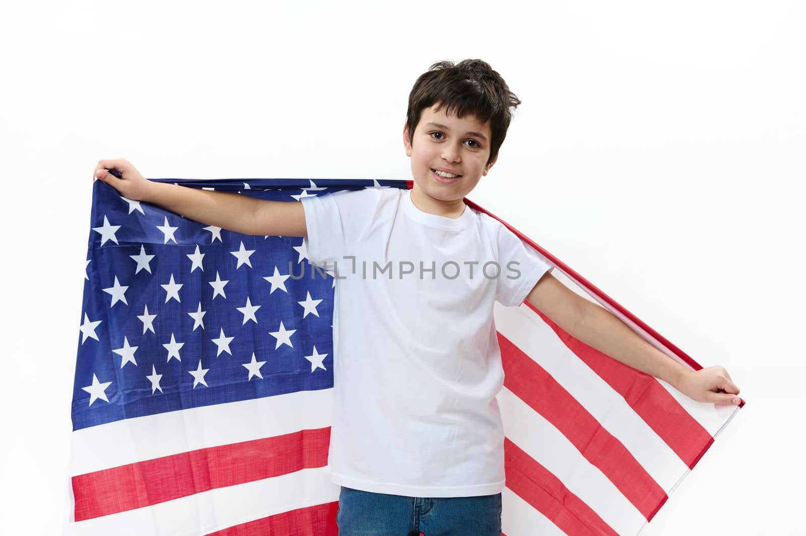 Happy American preteen boy in casual t-shirt and denim jeans, carries USA flag, celebrates Independence Day, July 4th. Citizenship, immigration, emigration, winning green card lottery, freedom concept