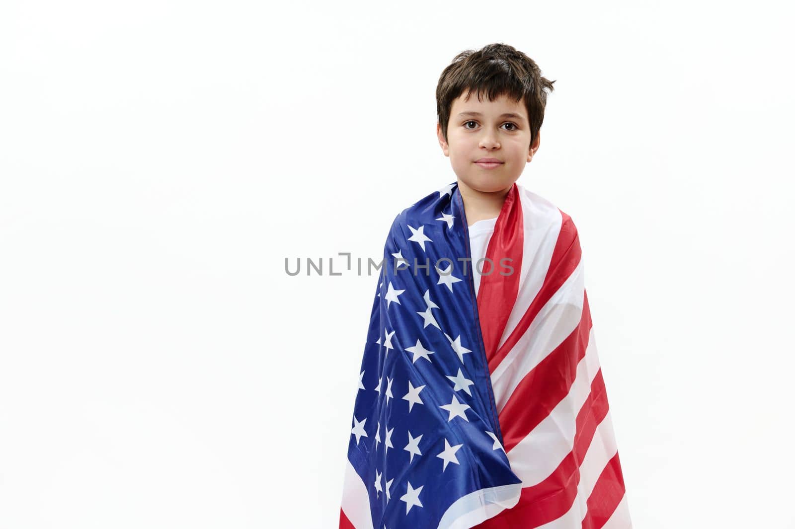 Confident American citizen, patriotic teenage boy wrapping in USA flag on the Independence Day of United States of America on July 4th, isolated over white background. Freedom and citizenship concept