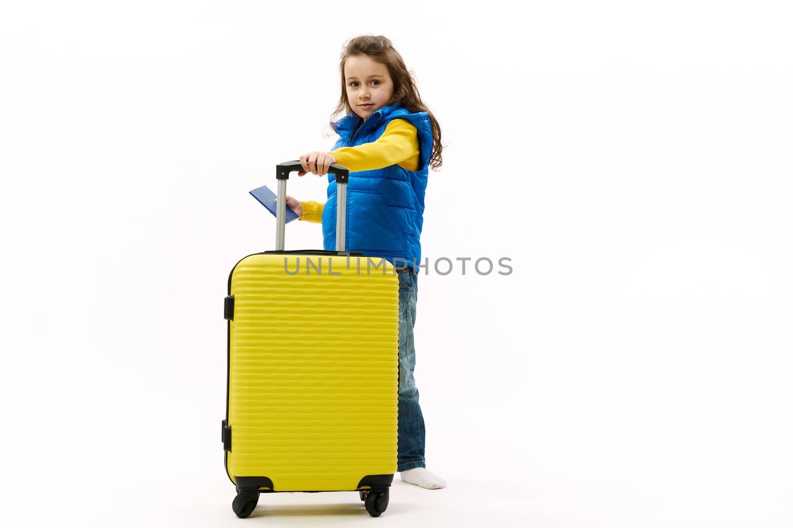 Traveler little child girl, in blue down jacket, with yellow suitcase and boarding pass, isolated on white background by artgf