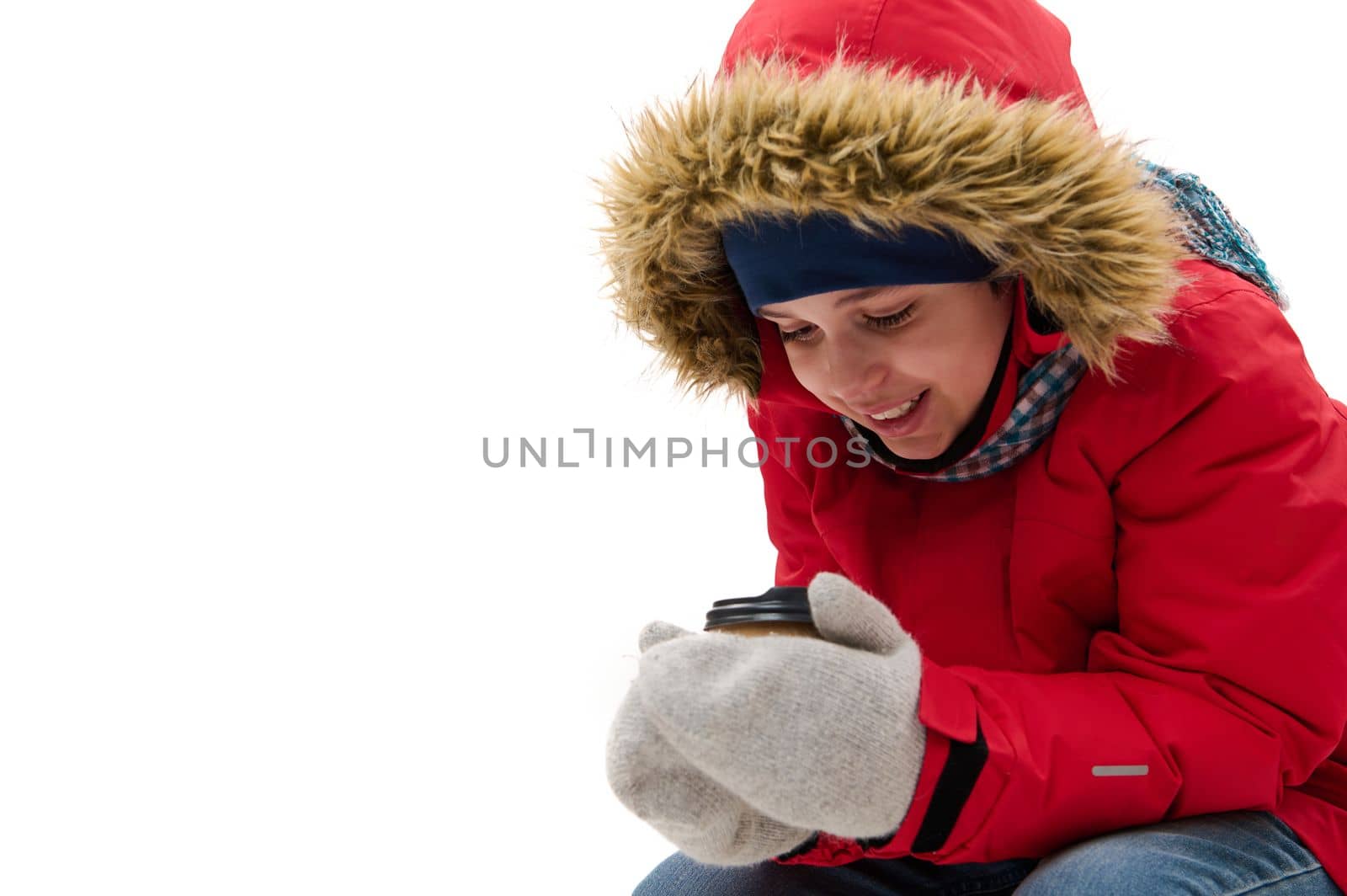 Preteen child boy, cute traveler adventurer in warm clothes, warming up, holding a disposable paper cup of hot drink, isolated over white background with free advertising space. Winter travel concept