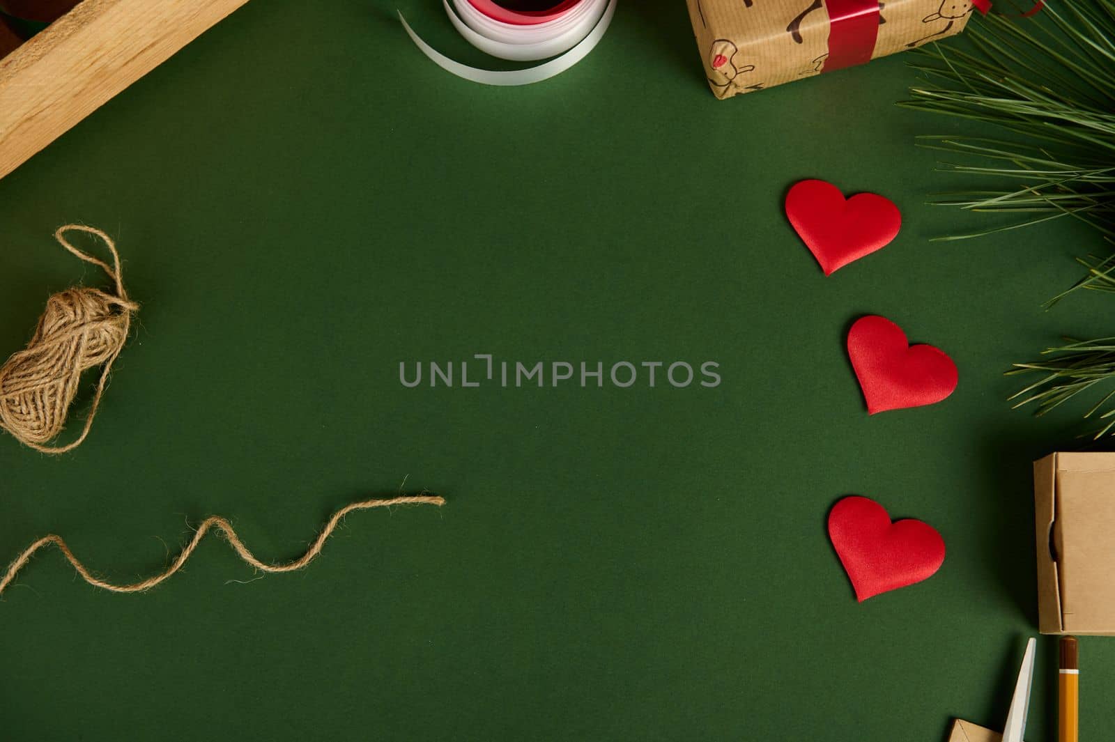 Top view of red decorative hearts, linen rope and wrapping materials on a green background with copy advertising space. Boxing day. Christmas mockup. Handwork art. Diy presents. Flat lay. Still life