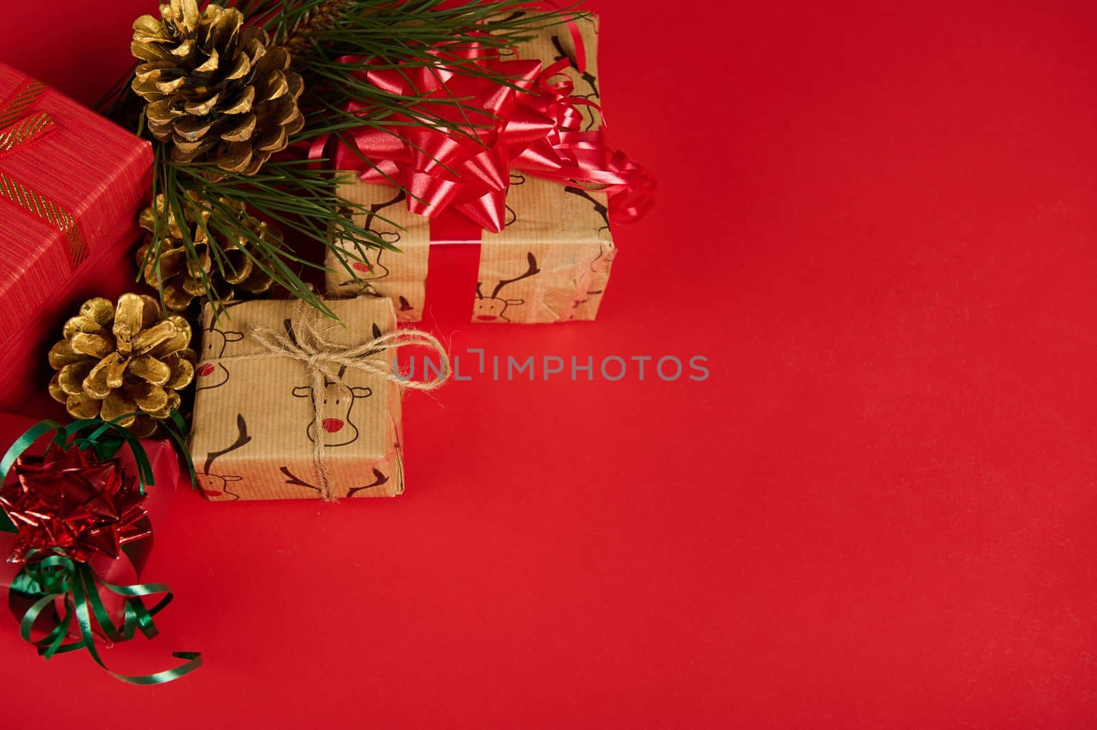 Christmas still life with gift boxed and golden pine cones in the corner of a red background with copy ad space for text. Mockup with cute presents, decorated with wrapping paper and satin shiny bows