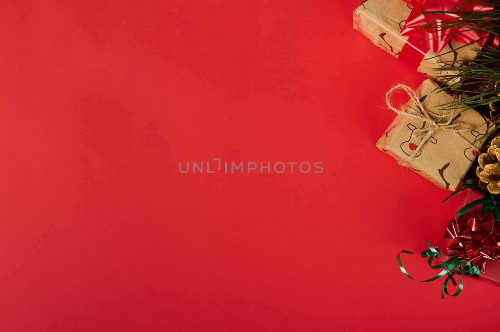 Partial view of Christmas gifts, wrapped in a wrapping paper with deer pattern and decorated with shiny ribbons and bows in the corner of a red background with copy advertising space. Mockup. New Year