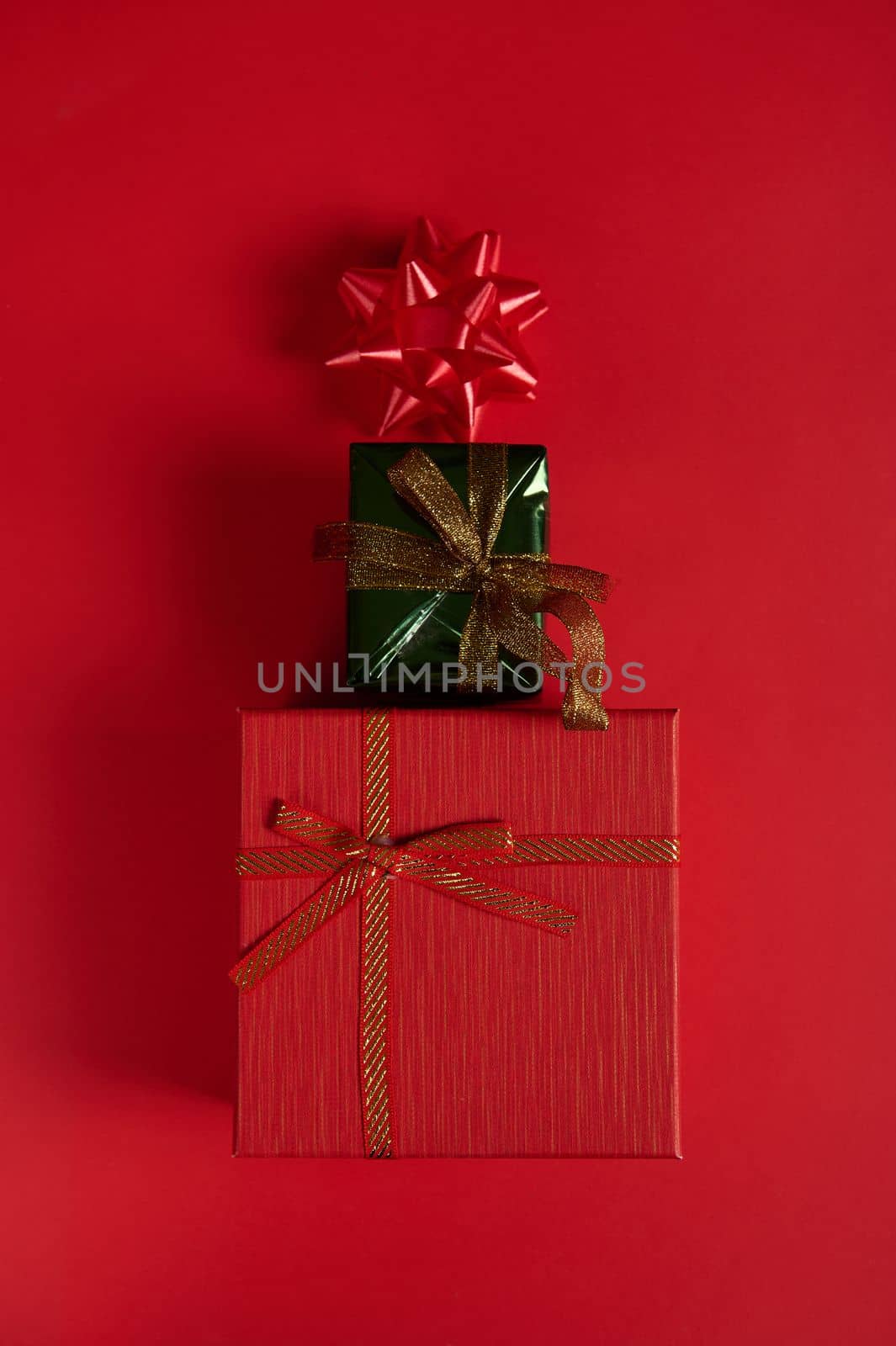 Flat lay. Vertical studio shot of cute stylish gift boxes, laid out in the shape of a Christmas tree, decorated with bow on red background. Still life. New Year's event. Boxing Day. December 25. Xmas