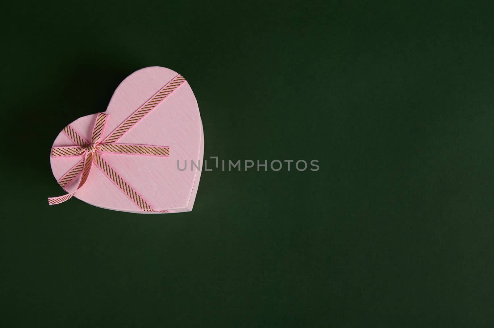 A romantic present, a heart shaped pink gift box with a cute surprise for Saint Valentine's or Women's Day, in the corner of a green backdrop with copy advertising space. February 14, March 08