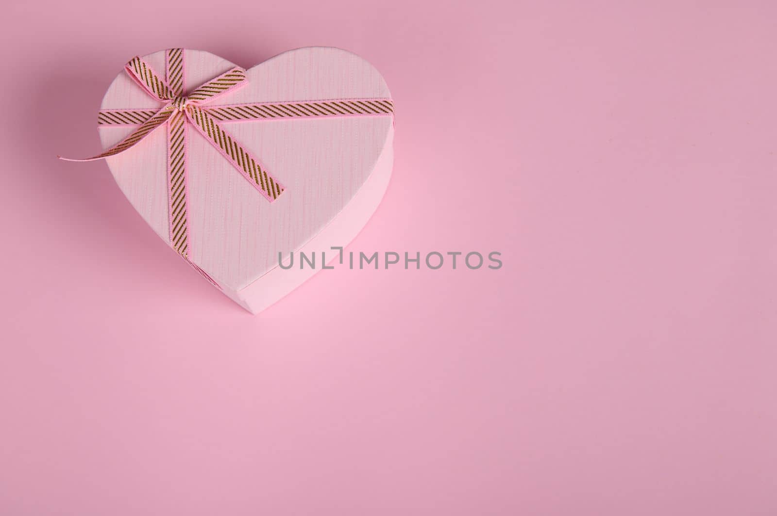 A romantic present, a heart shaped pink gift box with a cute surprise for Saint Valentine's or Women's Day, in the corner of a pastel pink background with copy advertising space. February 14, March 08