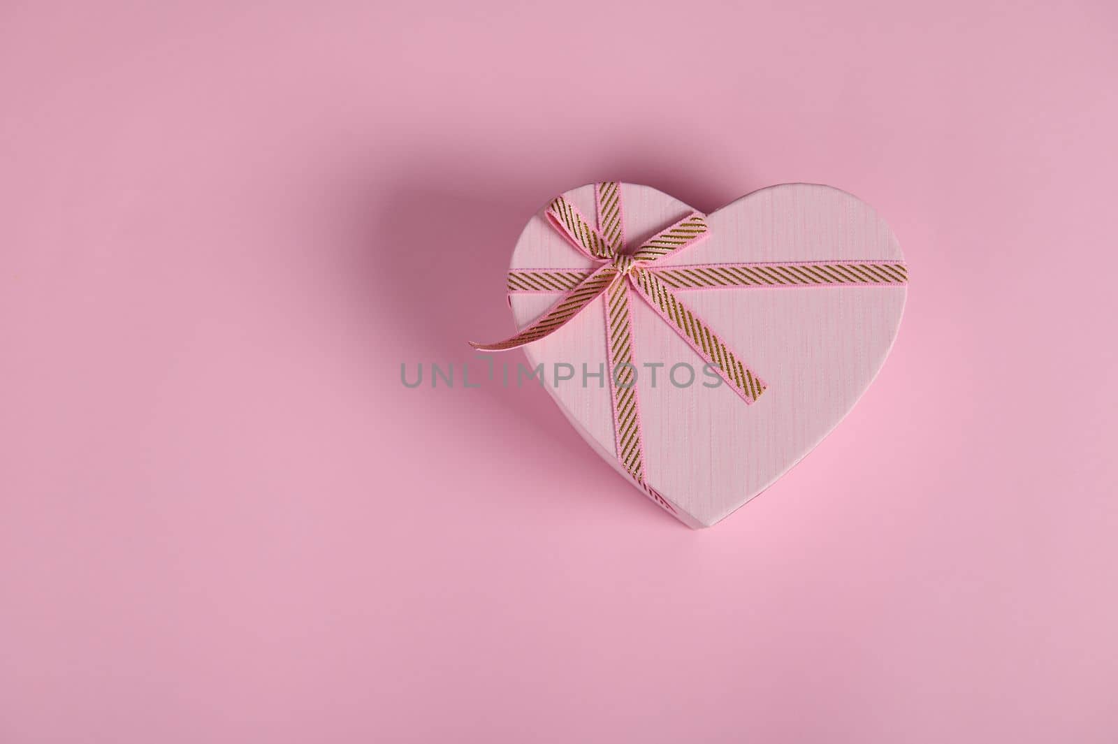 Still life. Monochrome flat lay composition with a heart shaped gift box with tied bow, isolated on pink background with copy advertising space. Romantic present for Saint Valentine's or Women's Day